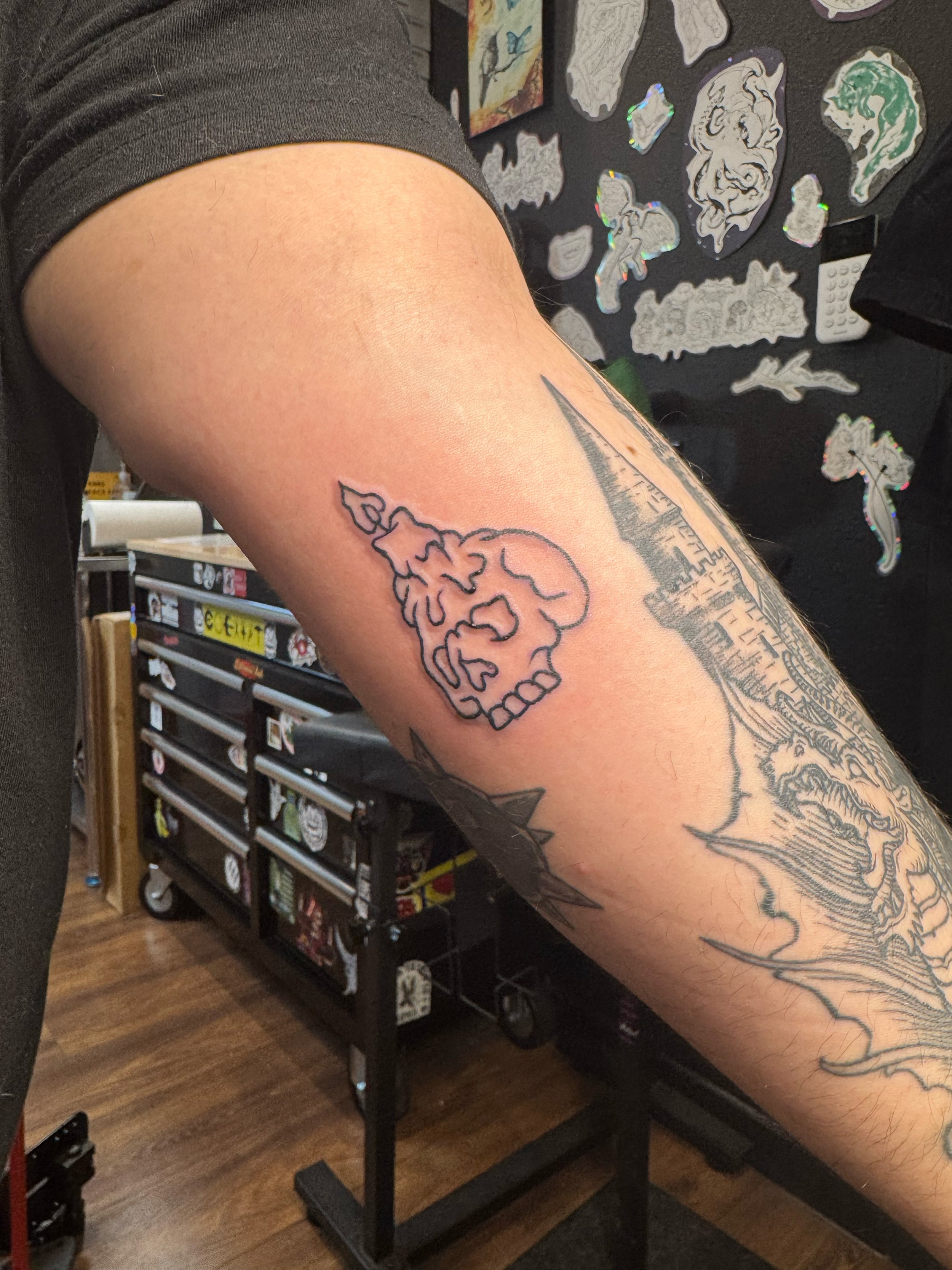 Tattoo of a stylized skull and flame design on a person's upper arm.