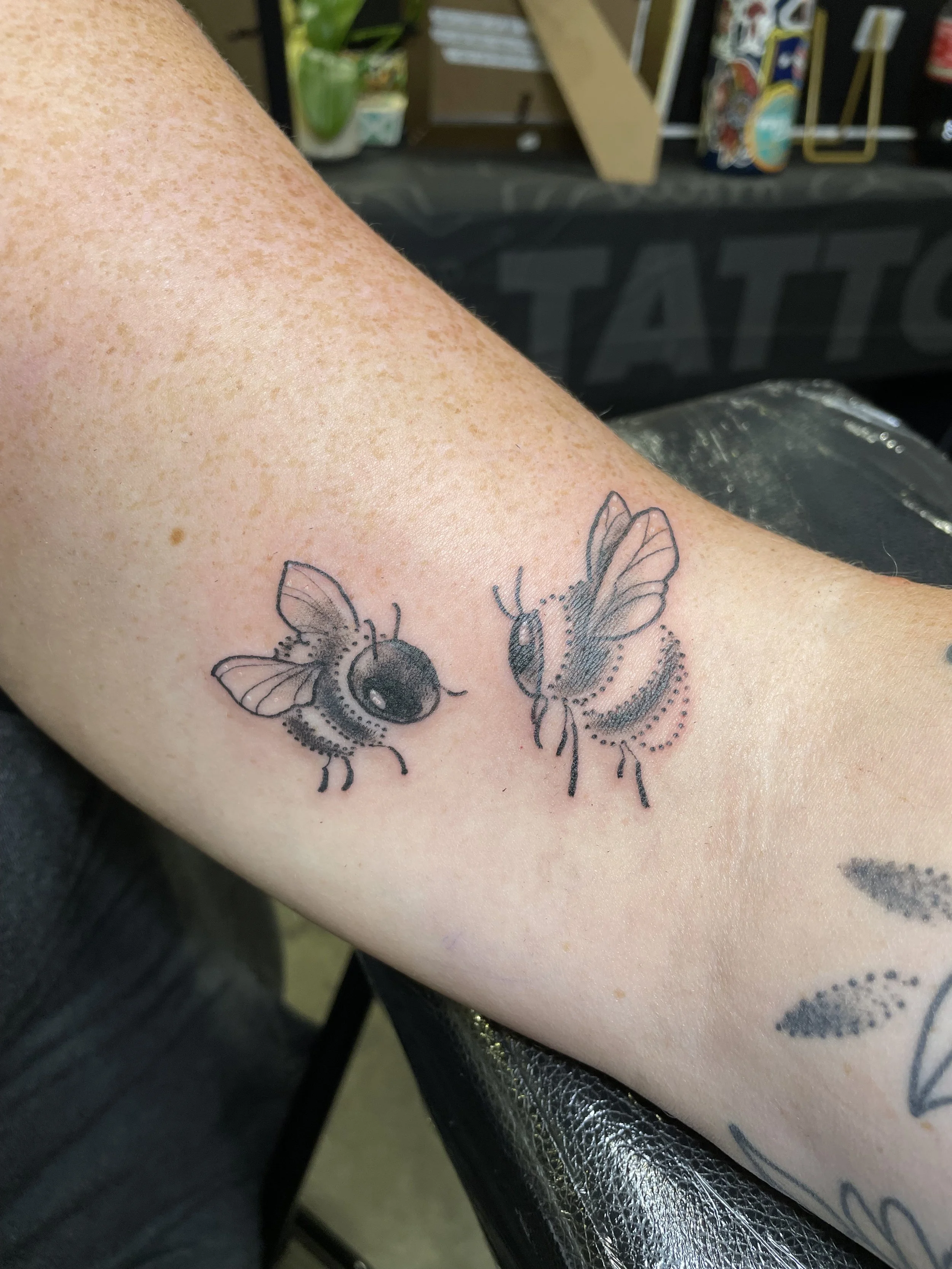 Tattoo of two bees on a person's inner arm, drawn in black ink with detailed wings and bodies.