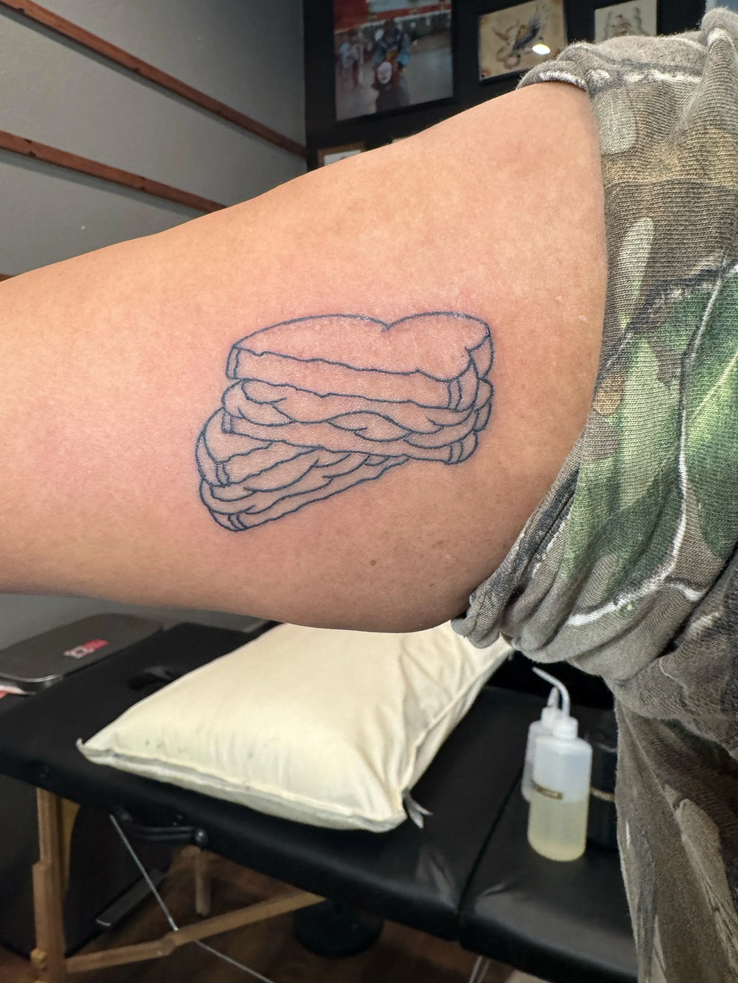 Line drawing tattoo of a stack of pancakes on a person's upper arm.