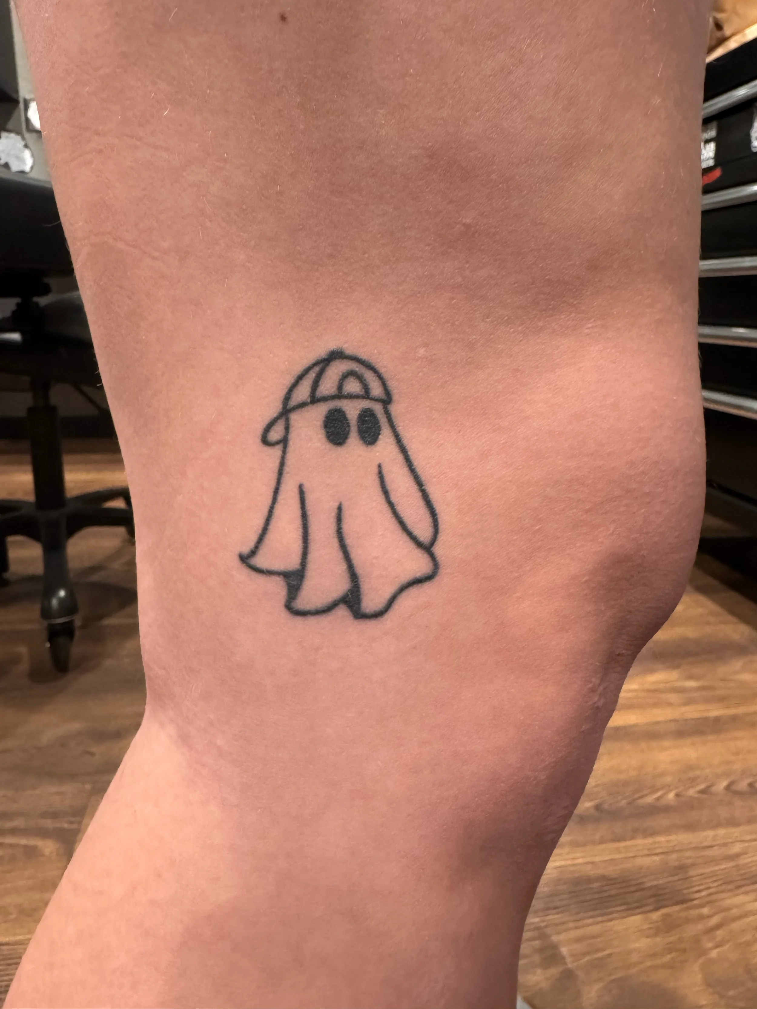 A small tattoo of a cartoon ghost wearing a cap on a person's upper thigh.
