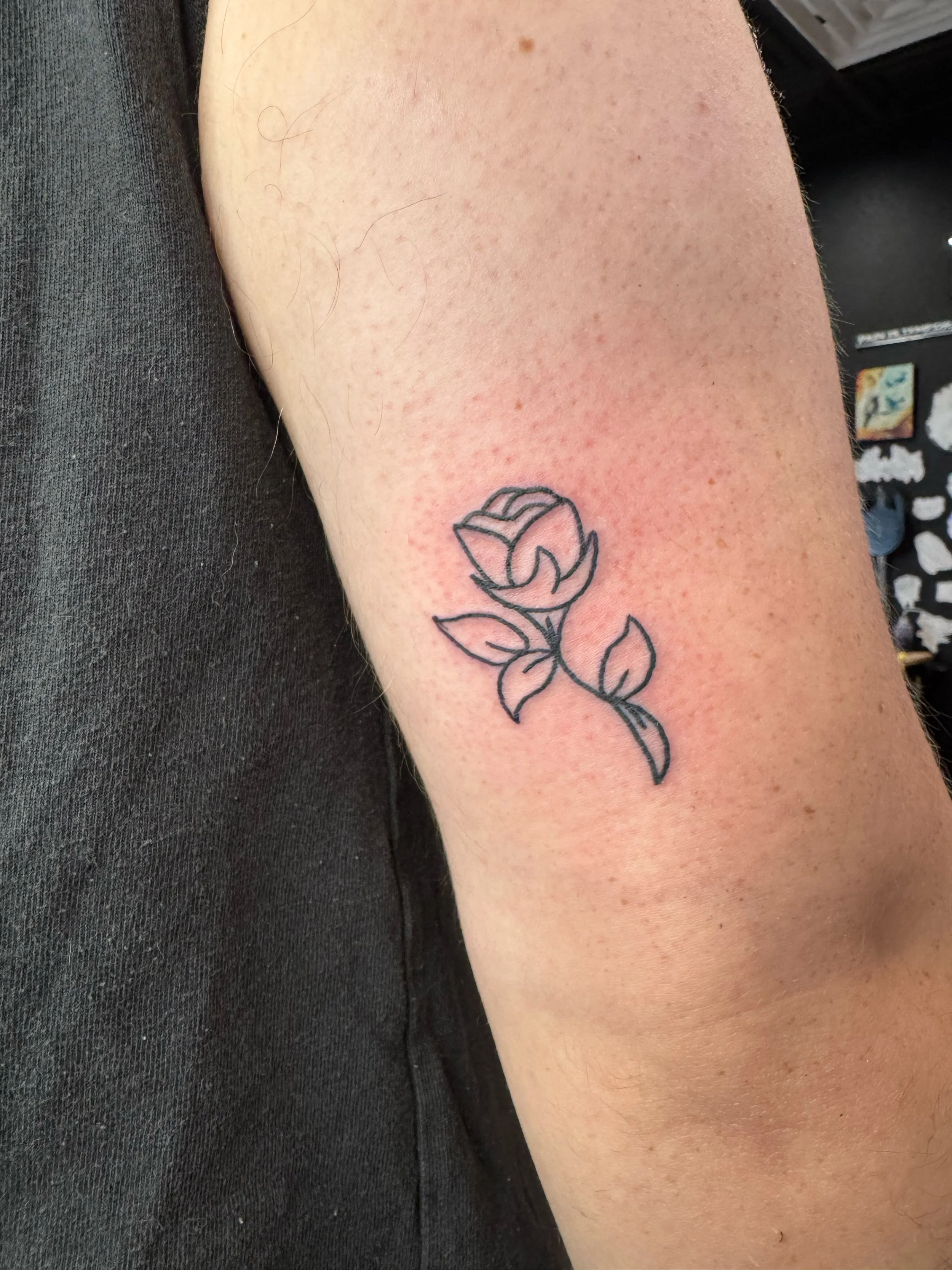 A minimalist black ink tattoo of a rose on a person's upper arm.