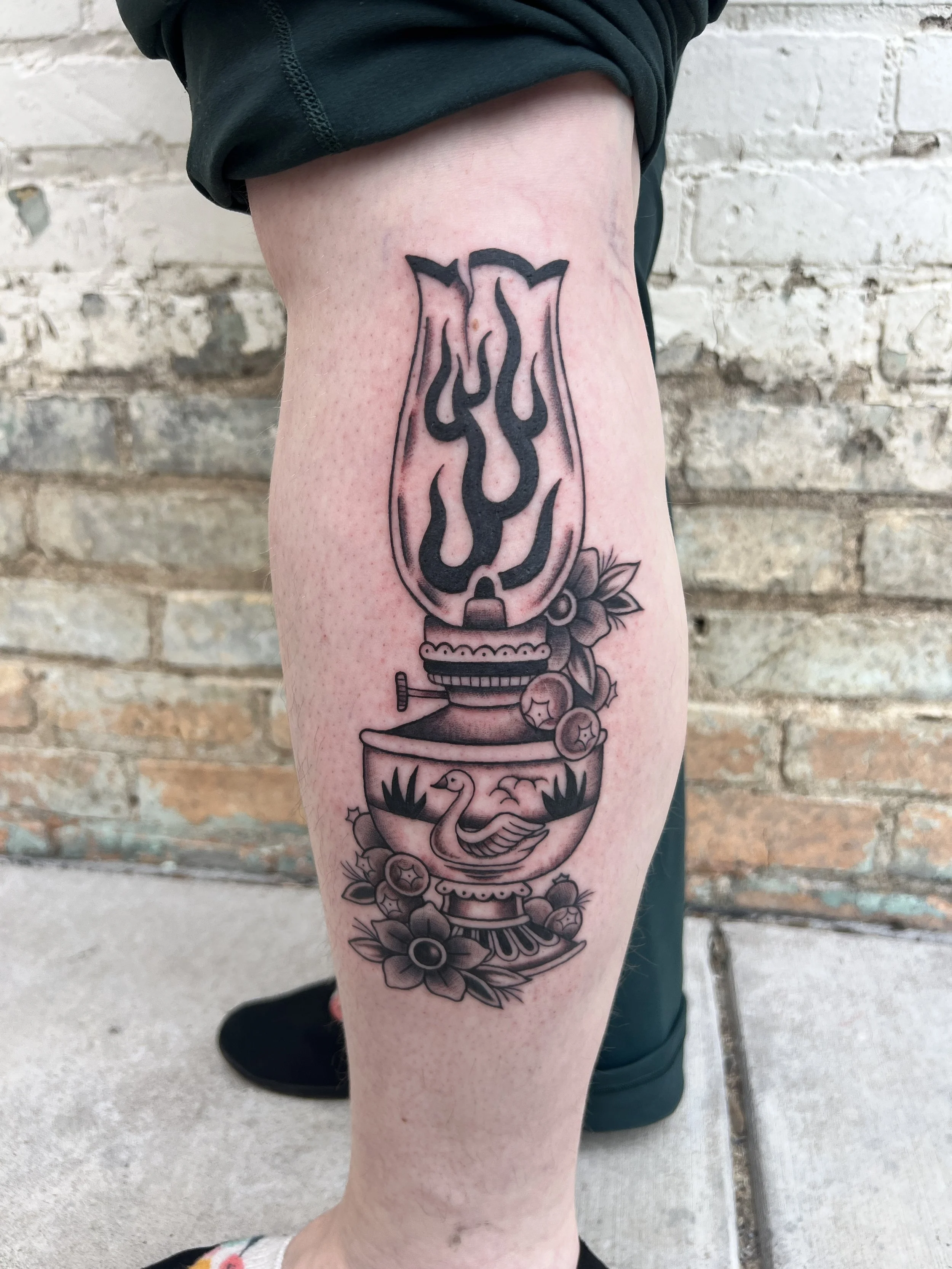 Tattoo of a vintage coffee grinder with flowers around it on a person's calf.