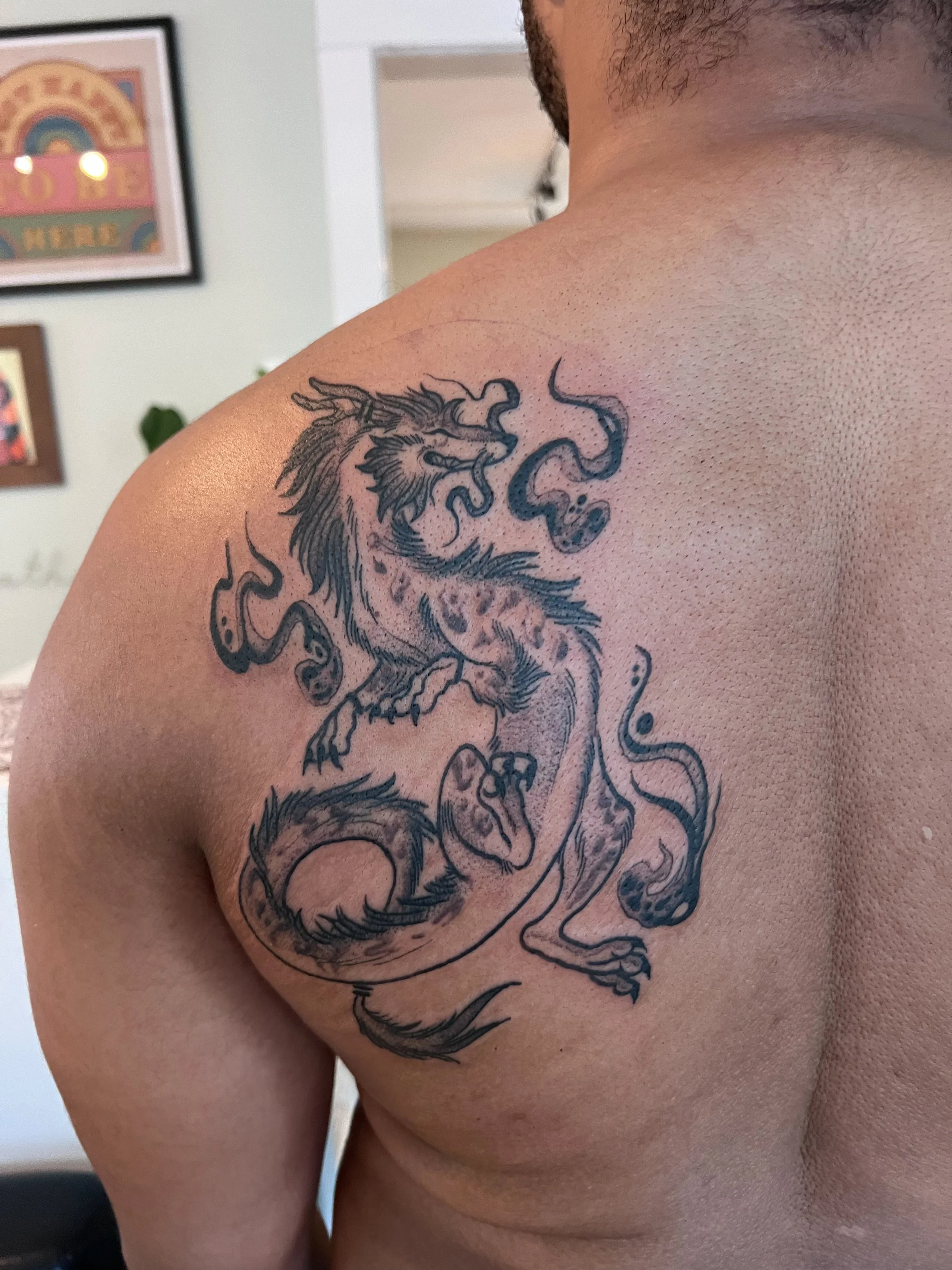 Tattoo of a dragon on a person's shoulder with detailed line work.