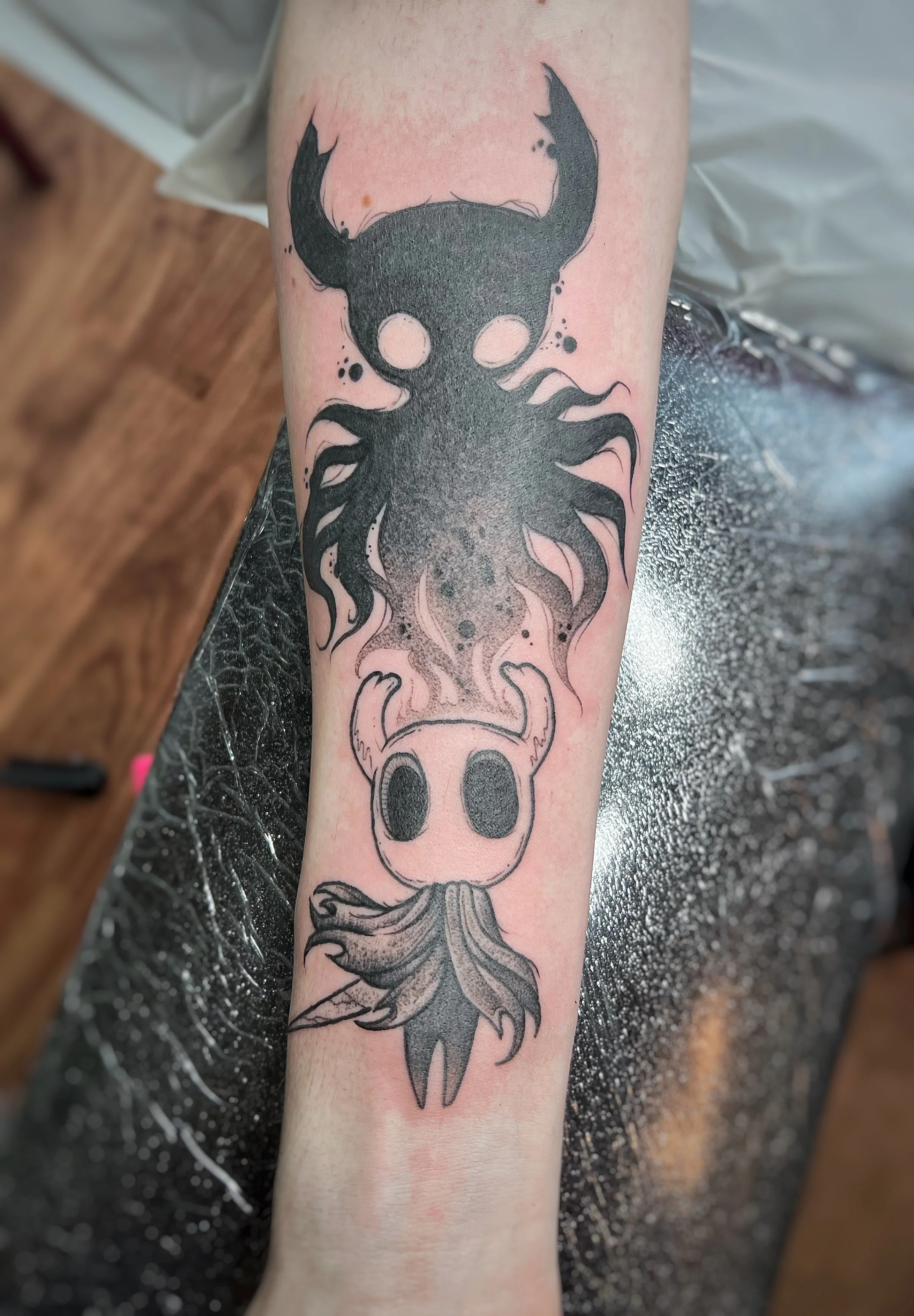 Tattoo of a black octopus with flames on the tentacles, positioned above a demonic skull with horns, on a person's forearm.