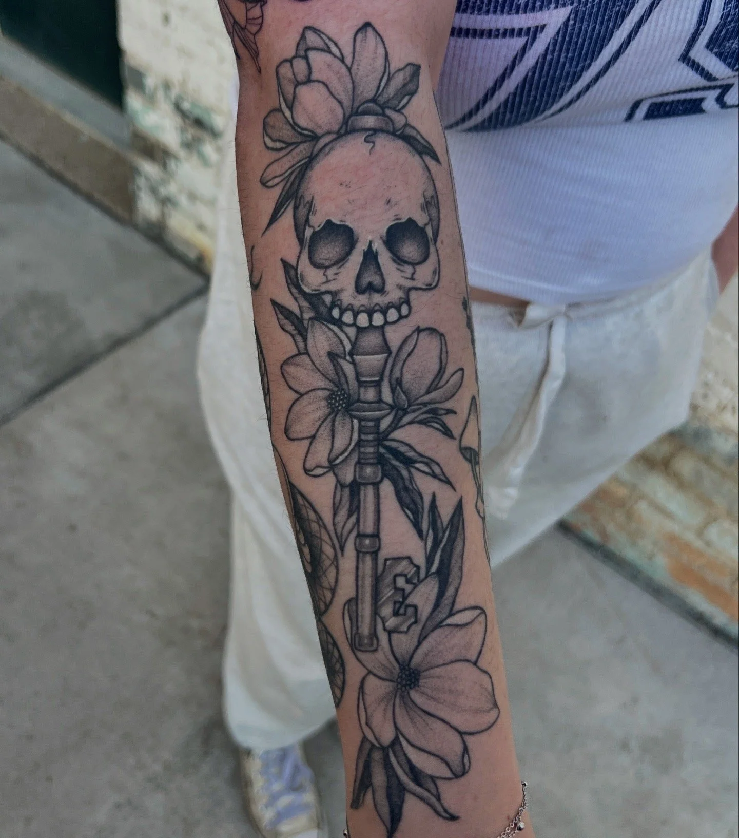 Tattoo of a skull with a flower on top, surrounded by leaves and a large flower near the wrist.