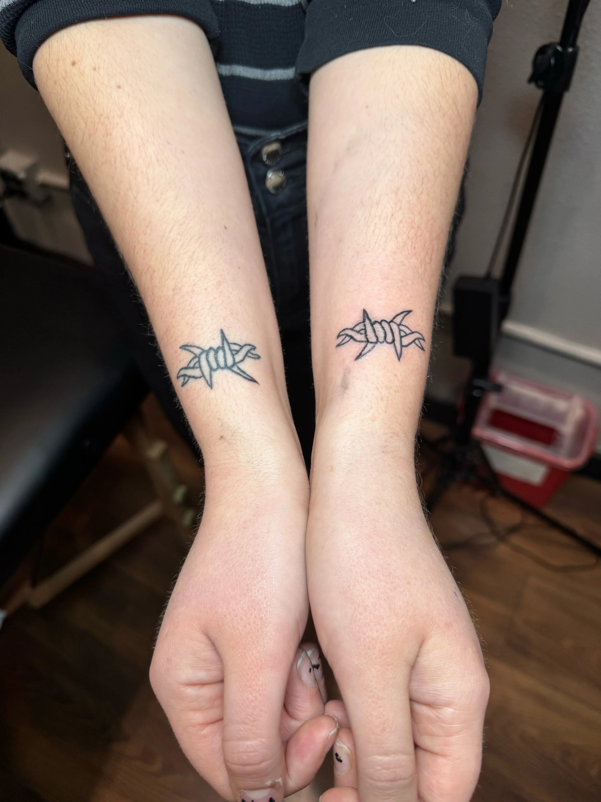 Tattooed wrists with barbed wire and handcuff design.