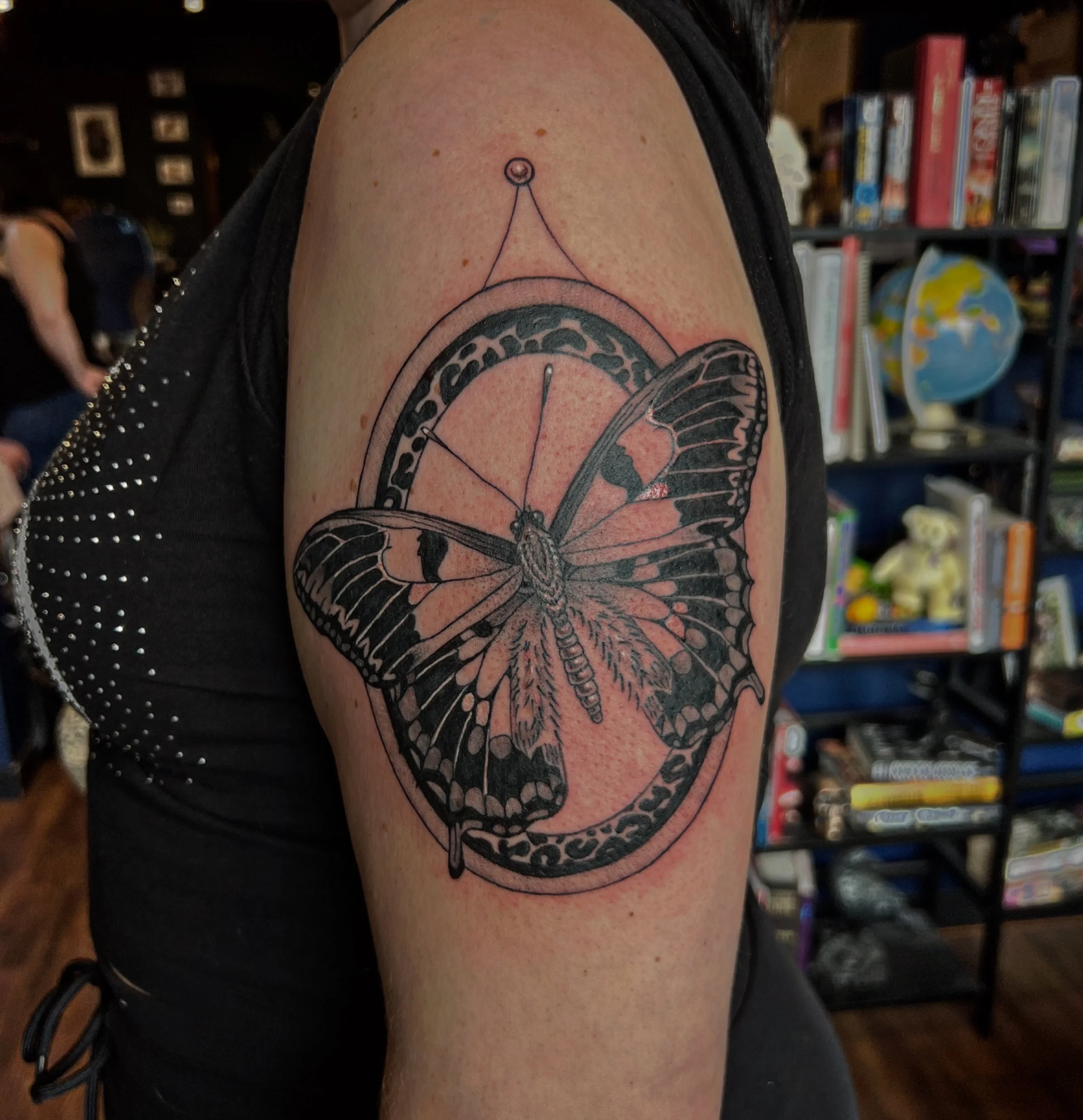 Tattoo of a butterfly with geometric and decorative elements on a person's upper arm, near the shoulder.