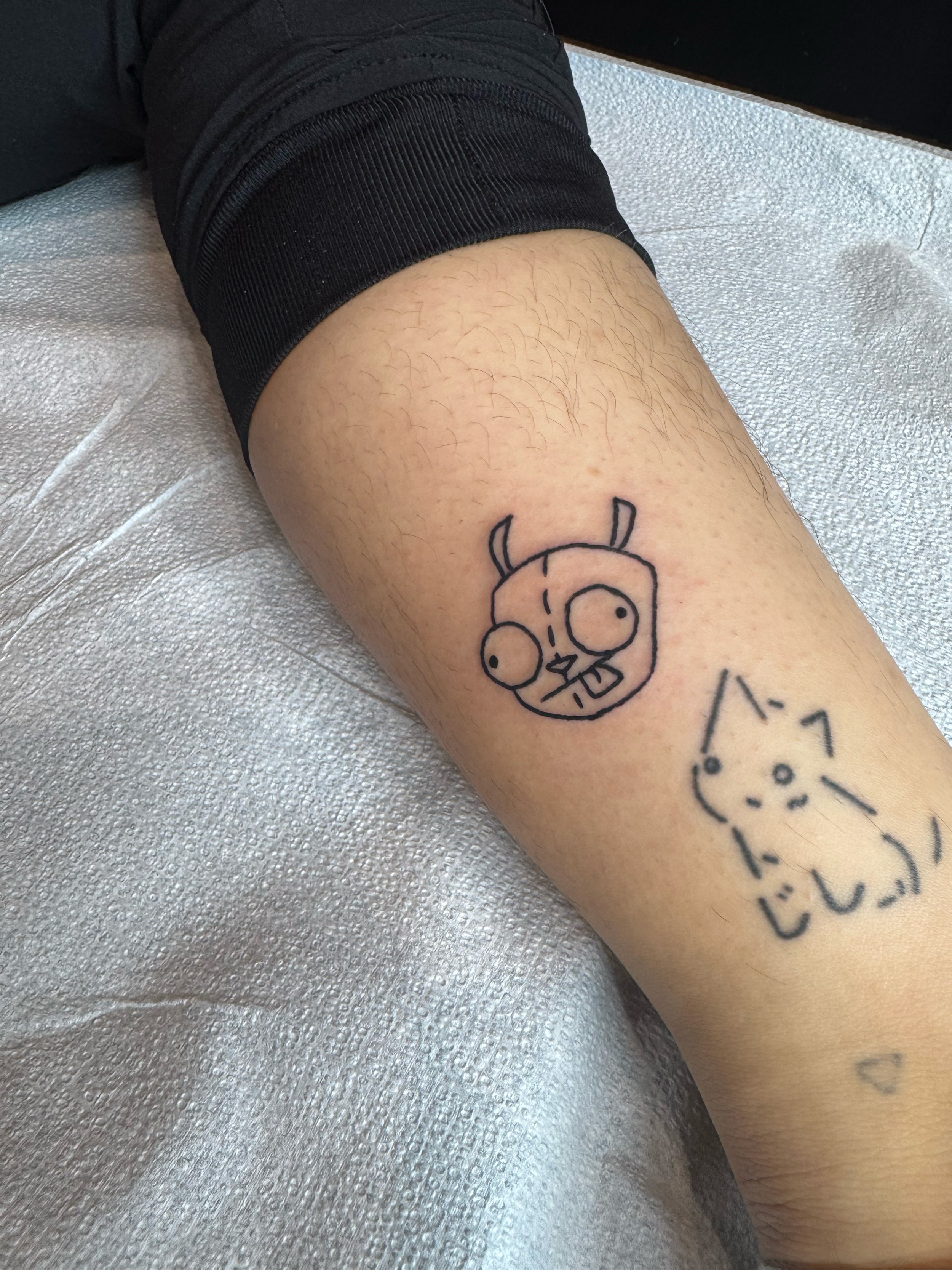 Tattoo of a cartoonish devil and a simple cat on a person's forearm.