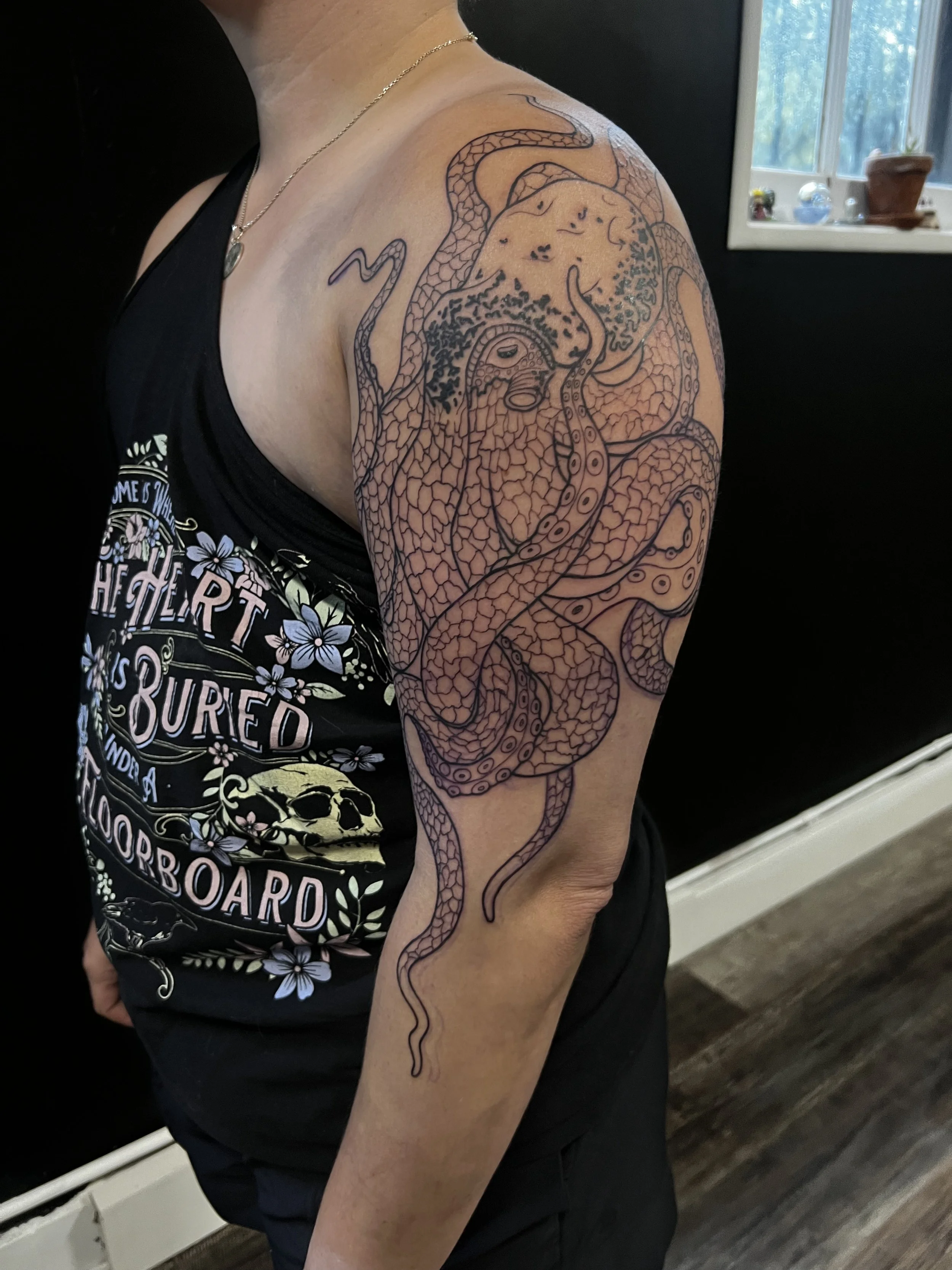 Black outline tattoo of a snake wrapped around a panther's face on person's upper arm, with a background of black wall and window showing trees.