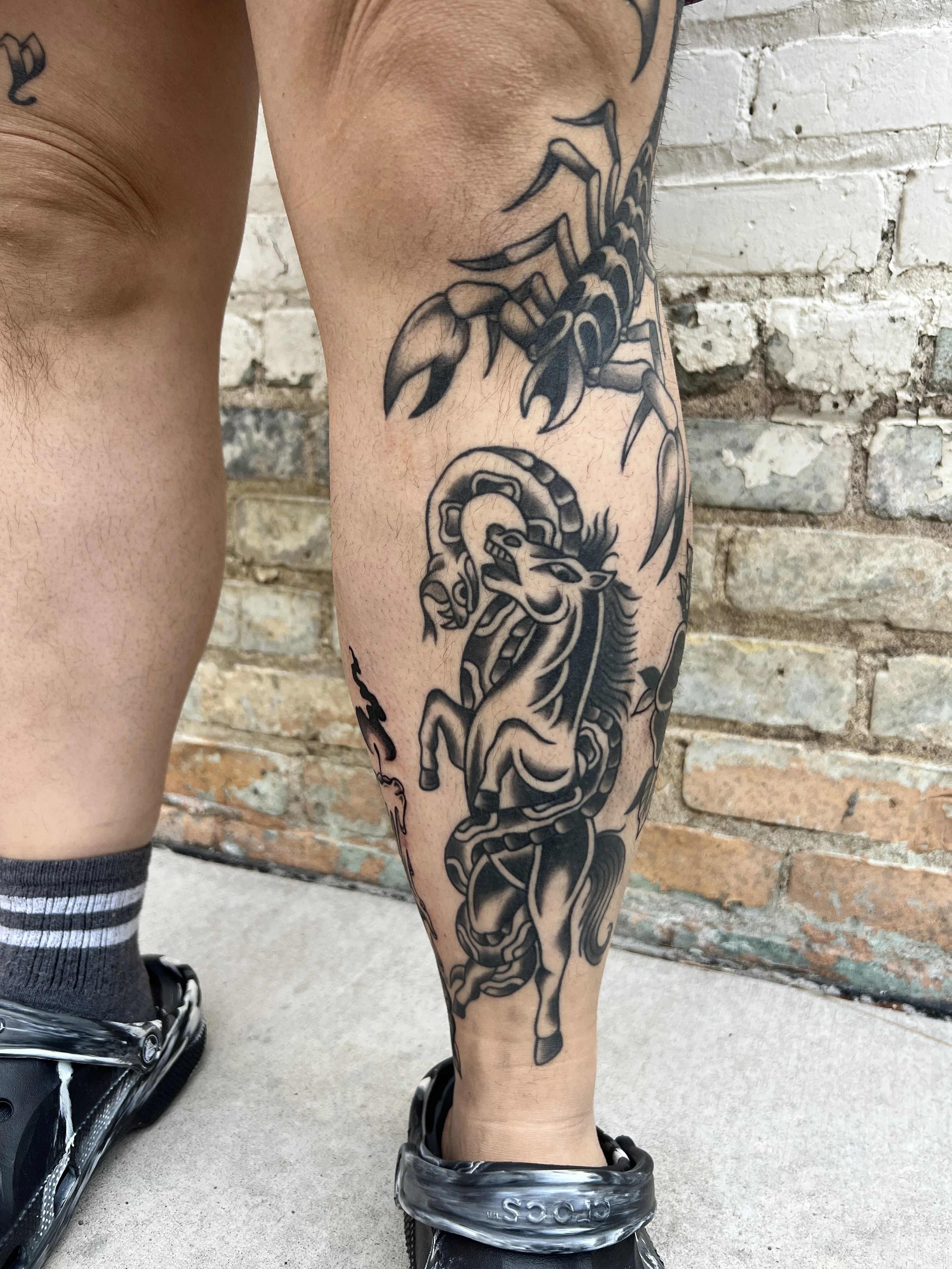 Tattooed arm with a scorpion and a snake against a brick wall background.