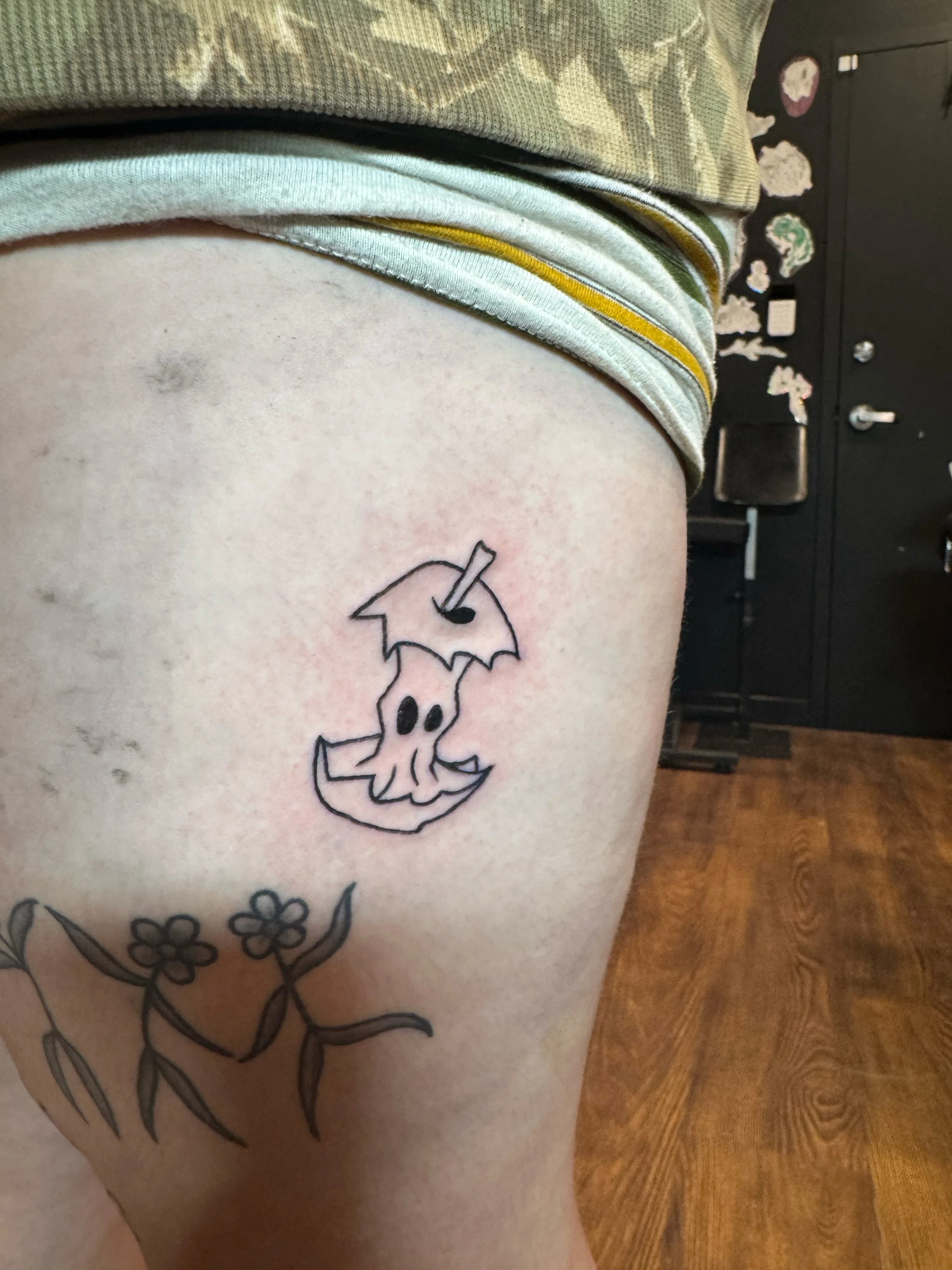Tattoo of a cartoon ghost holding an umbrella on the person's thigh.