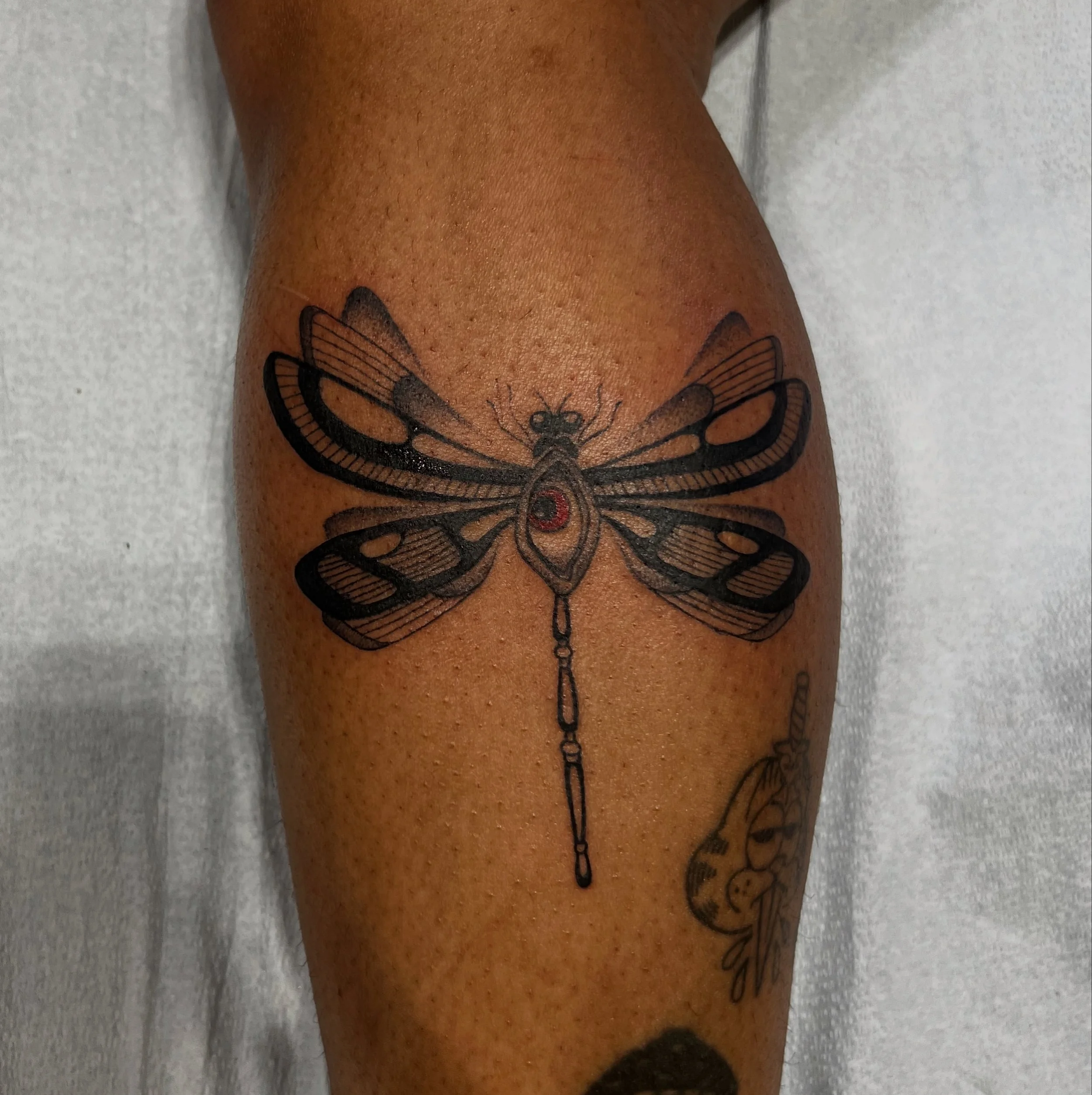 Close-up of a person's leg with a butterfly tattoo on the thigh, lying on a white surface.