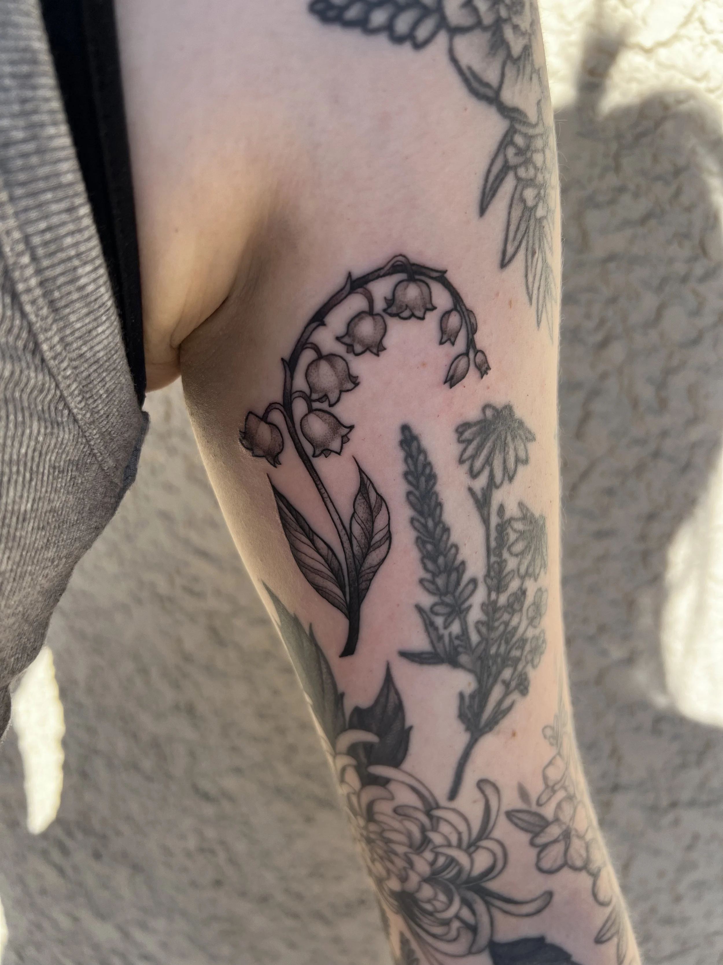A close-up of a arm with a detailed black and gray floral tattoo, featuring various flowers and stems.