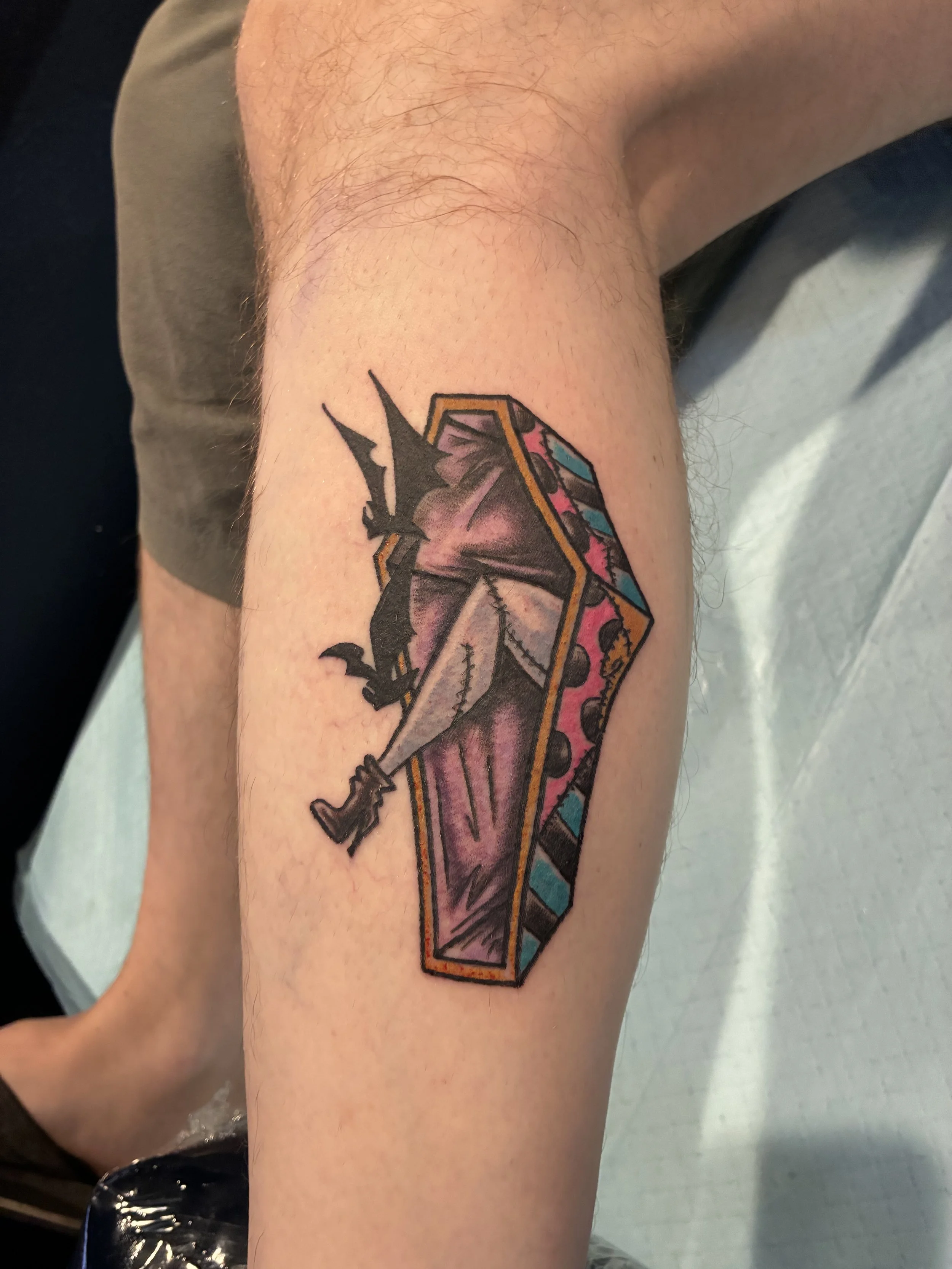 A colorful tattoo of a black dragon biting a Pinball Machine, with vivid pink, blue, yellow, and purple details, on a person's arm.