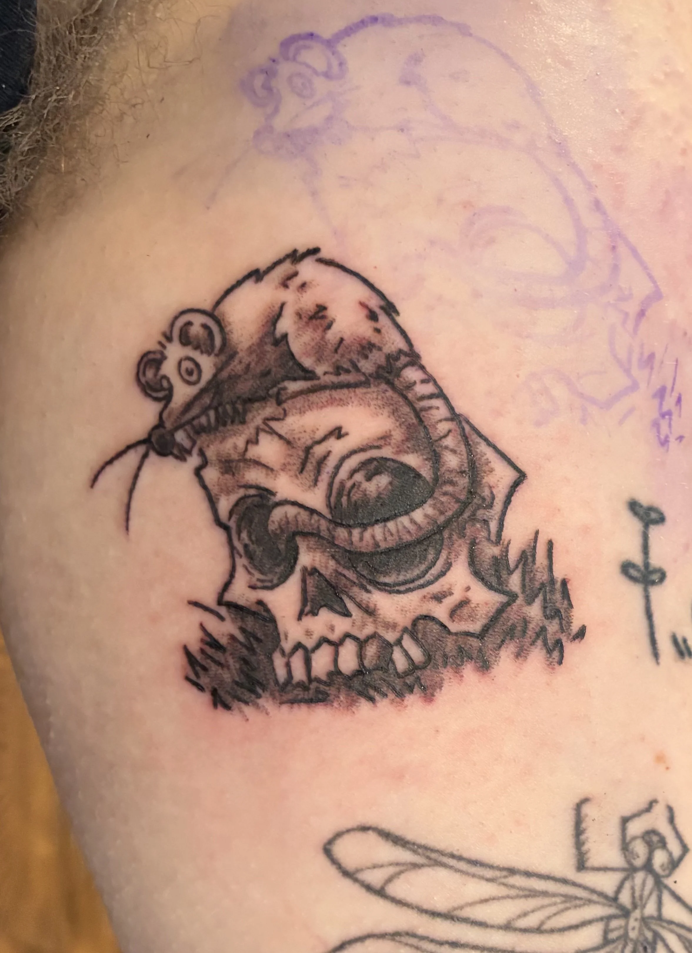 Close-up of a person's skin with a tattoo of a lion's face above a flower design and a faint purple outline of a lion's face in the background.