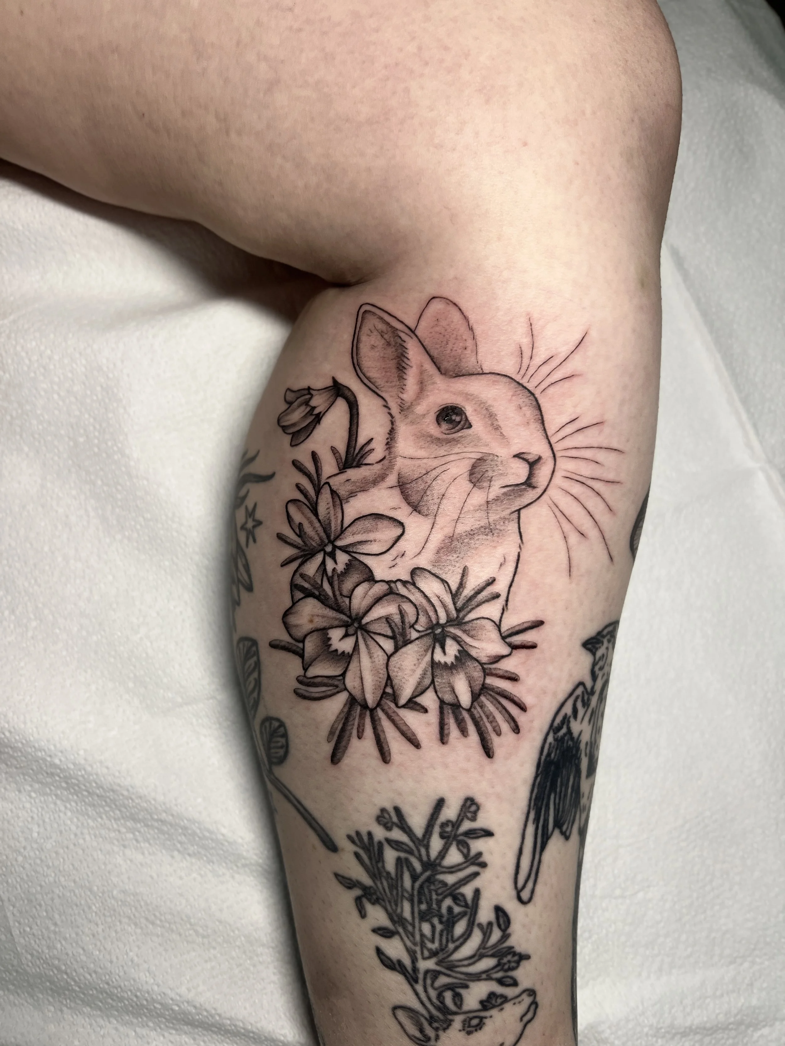 Tattoo of a rabbit's head, surrounded by flowers and leaves, on a person's leg.