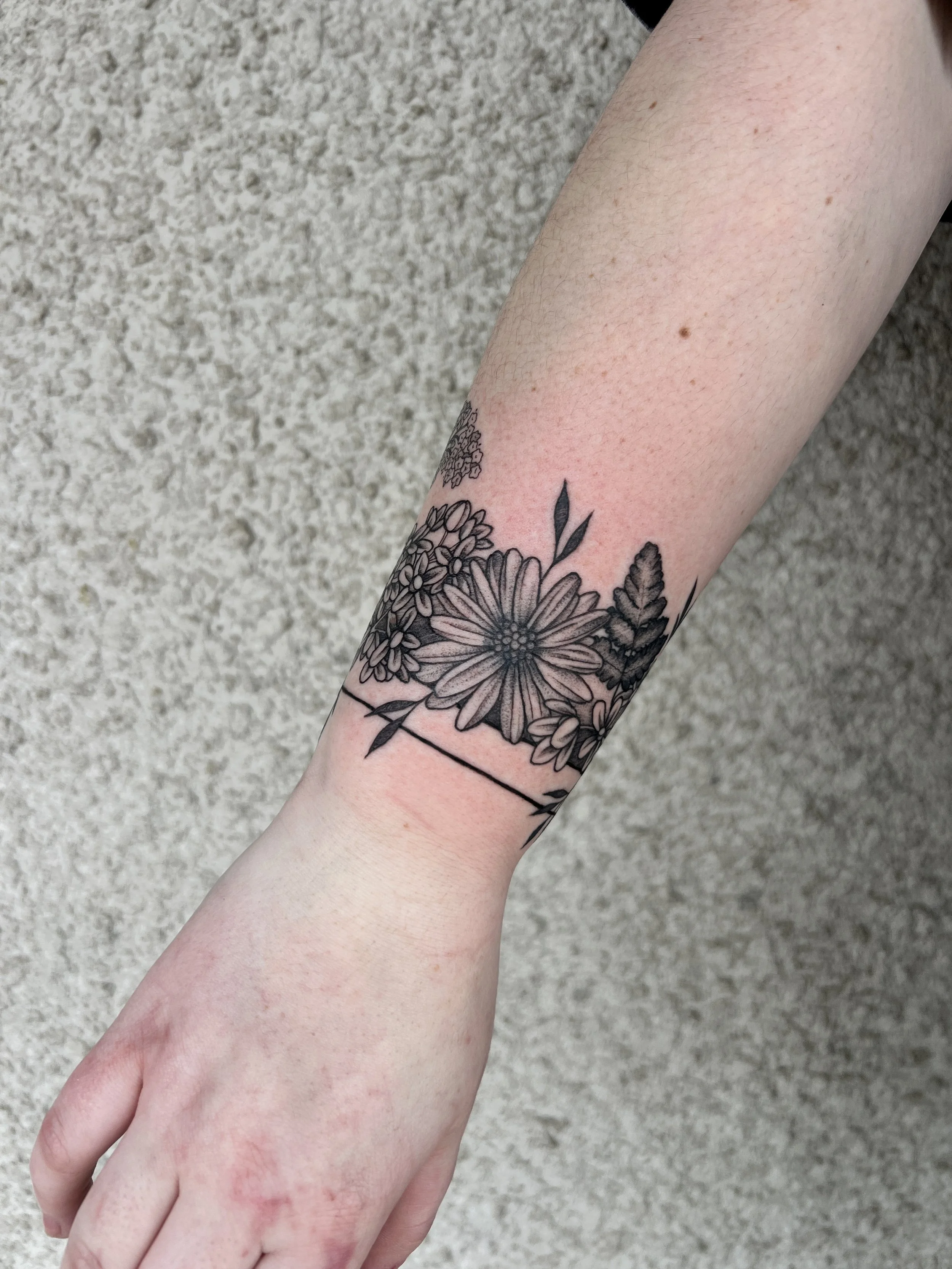 A person's arm with a floral tattoo on the forearm, standing against a textured beige wall.