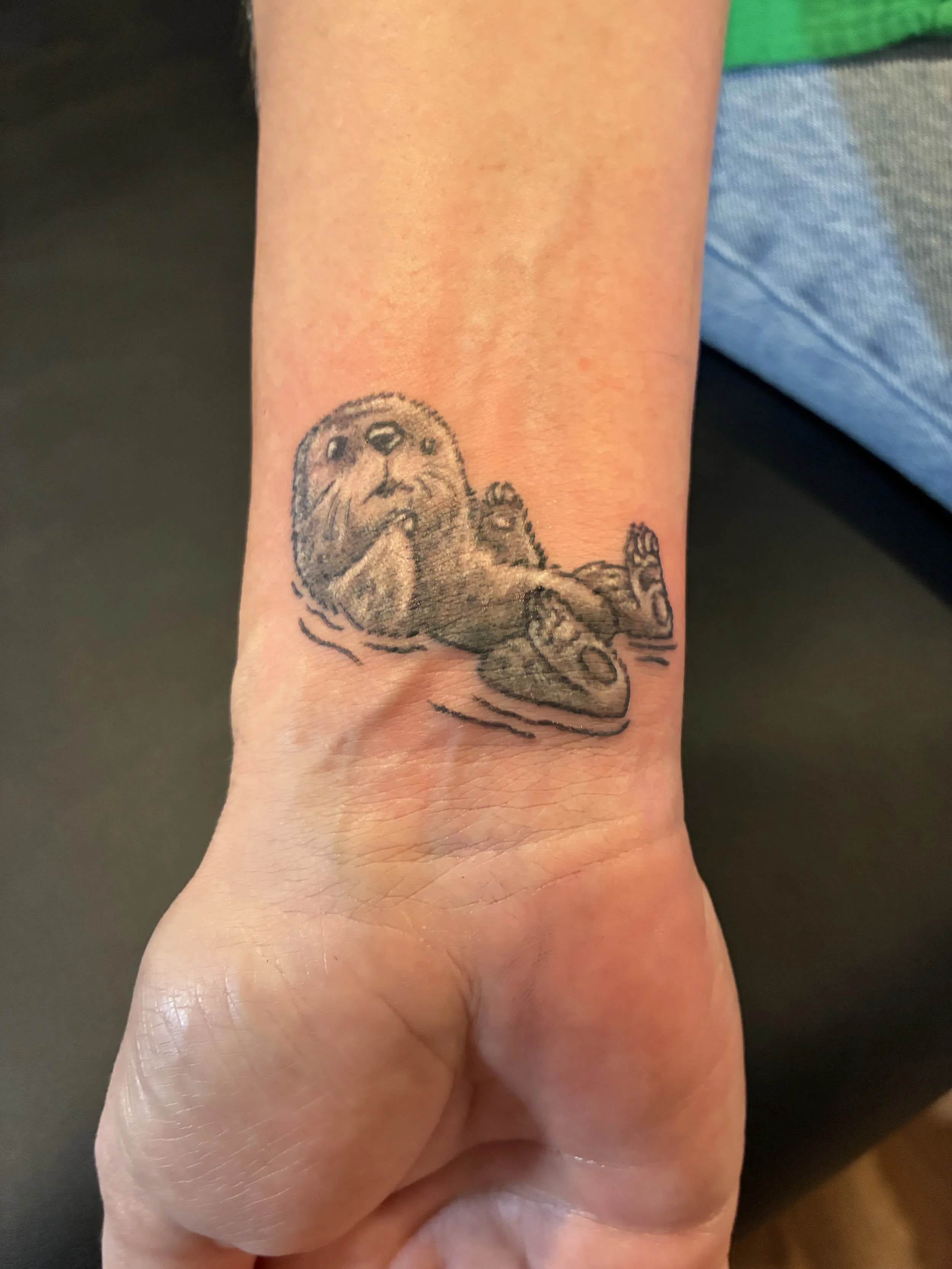 Tattoo of a baby otter on a person's wrist.