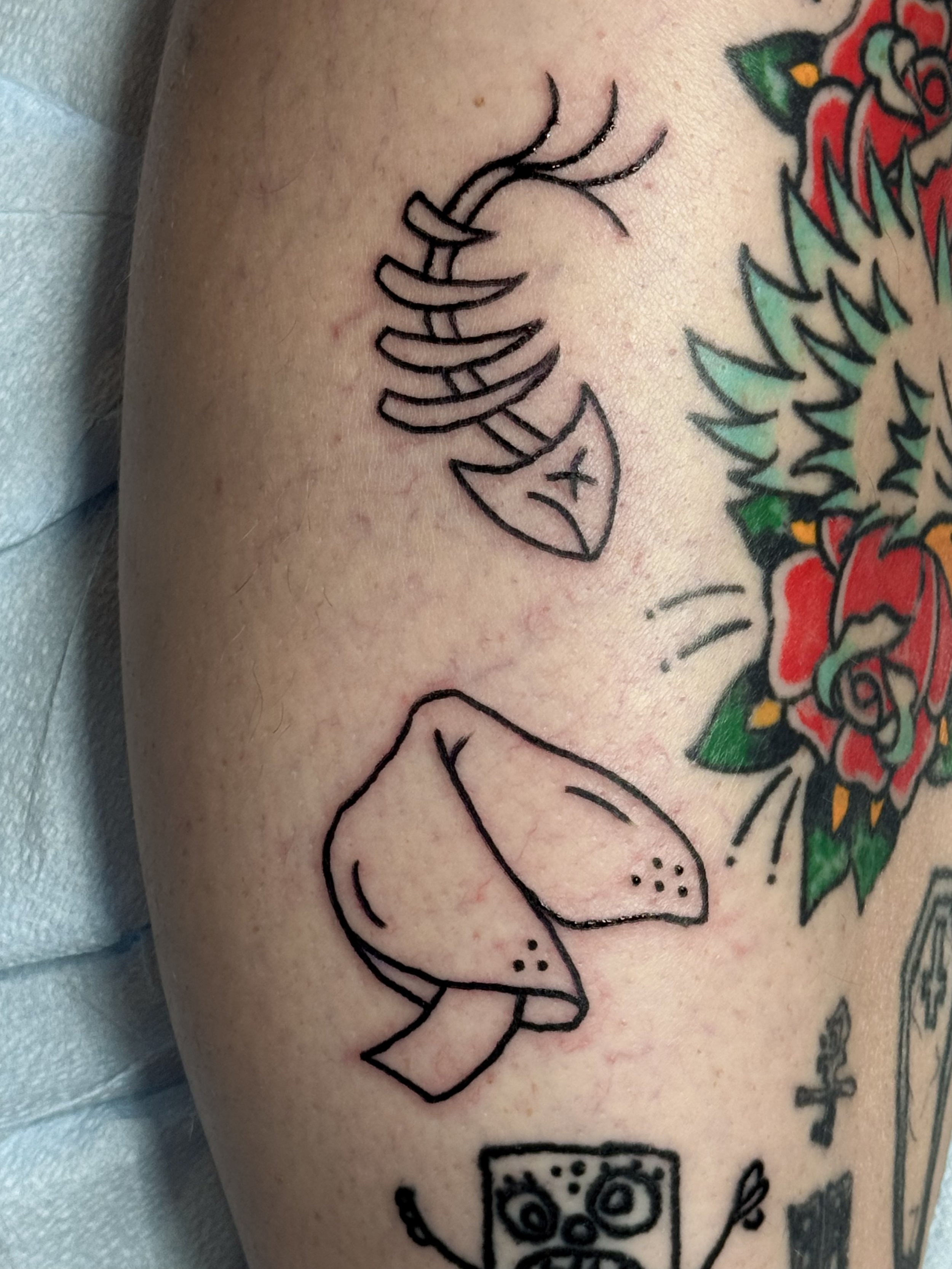 Close-up of a tattoo on skin that depicts a stylized, minimalistic fish with an abstract pattern and a fish hook intertwined with the fish.