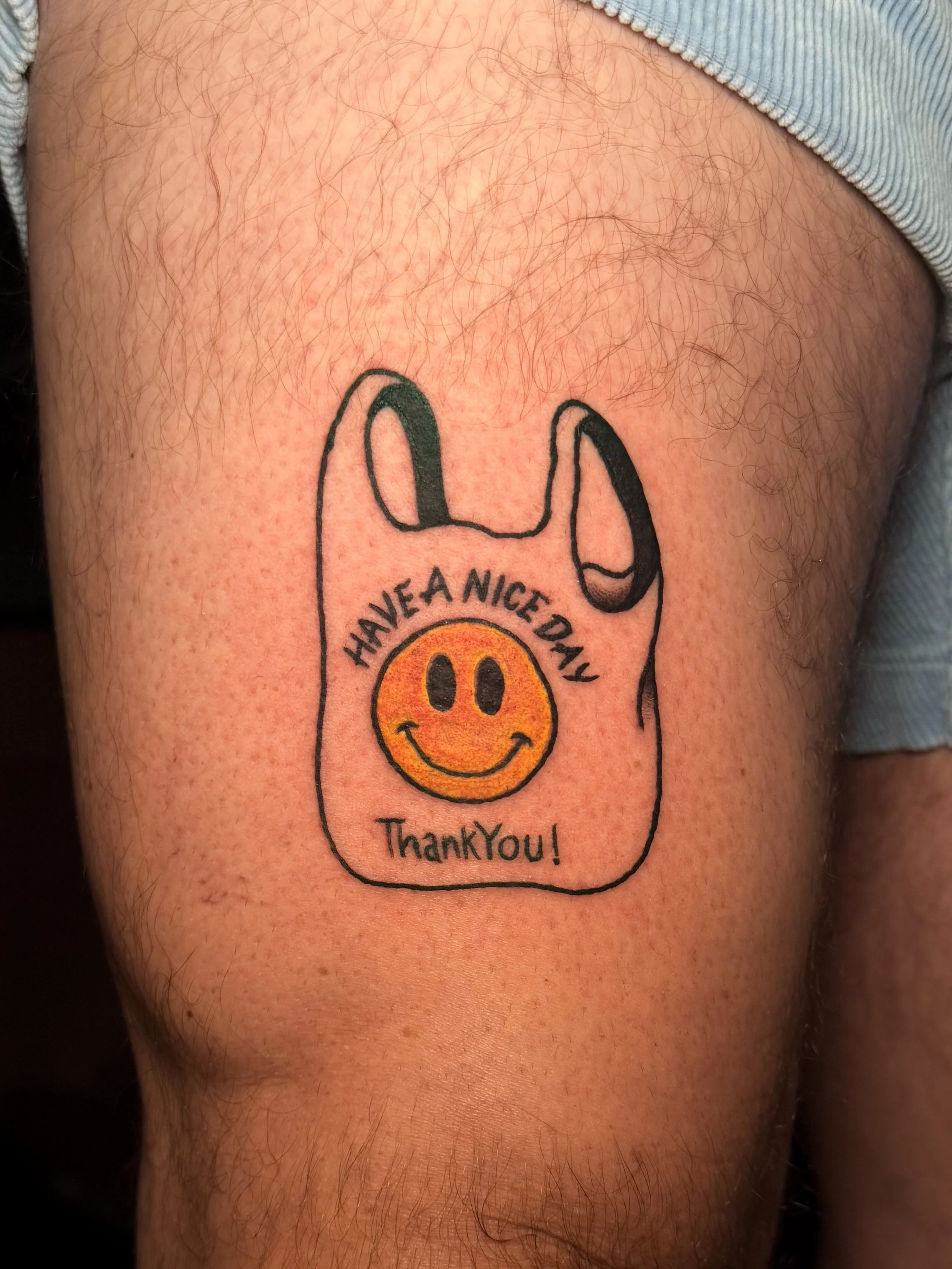A tattoo of a thank-you message with a smiley face on a person's upper arm.