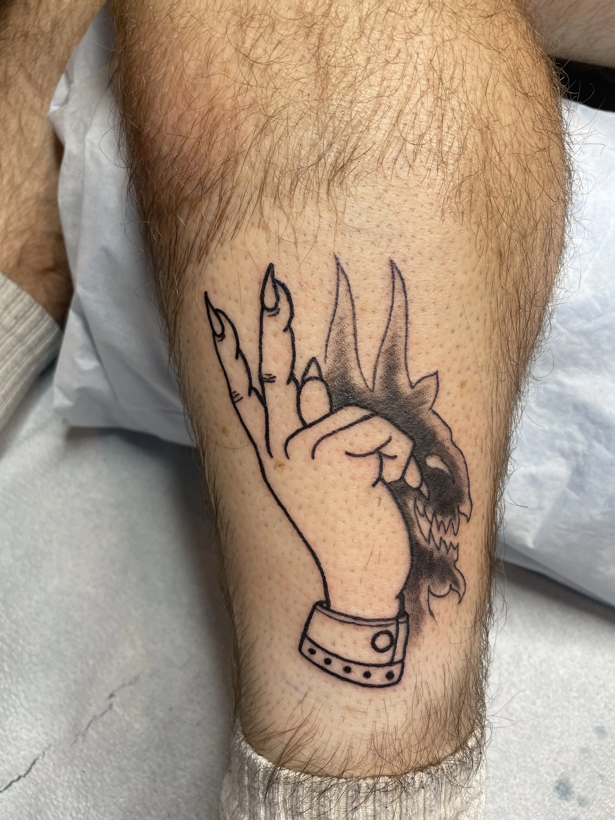 Tattoo of a hand with fingers extended, merging into a snarling wolf's head, on a person's upper arm.