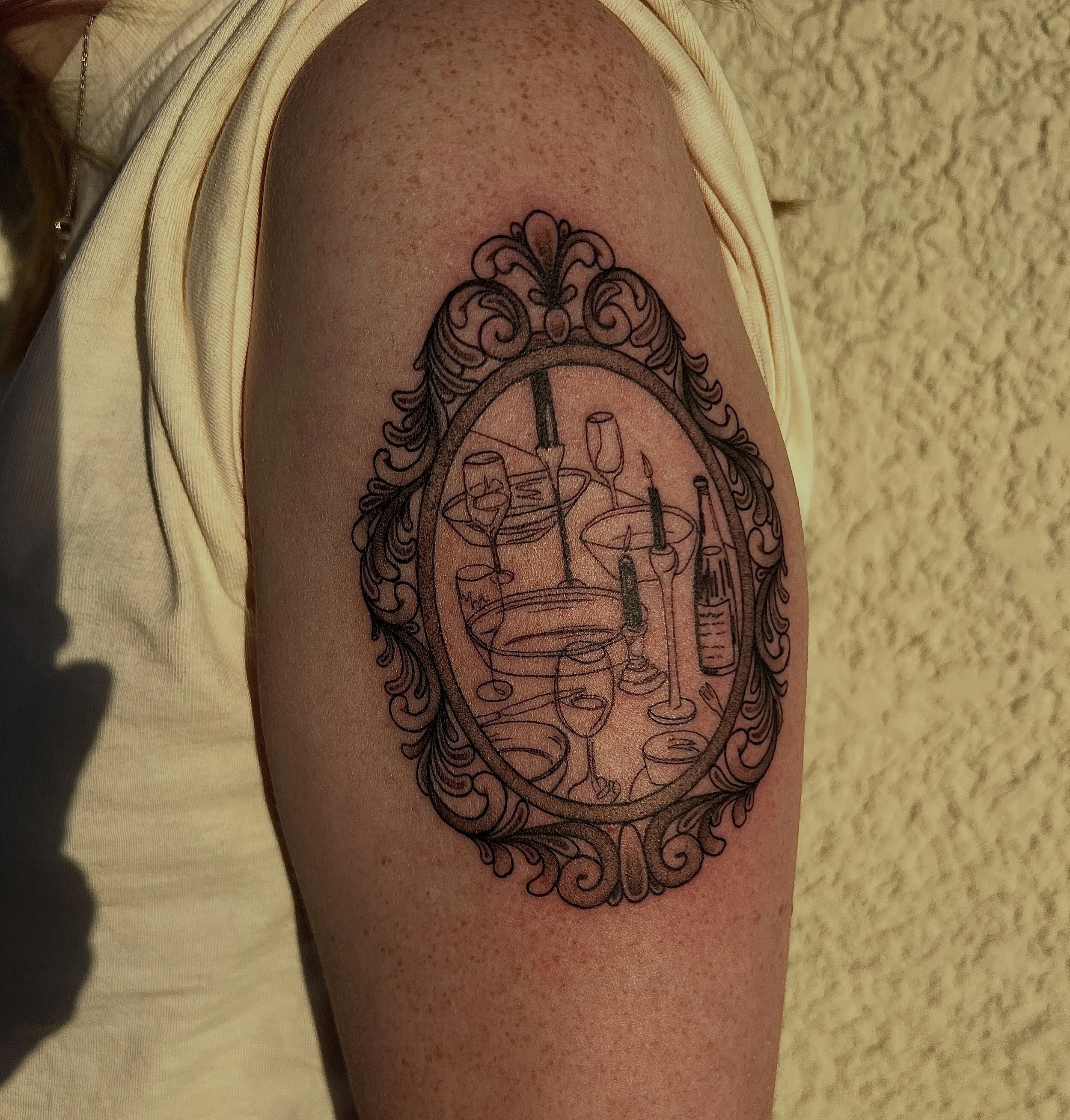 Close-up of a person's thigh with freckles and a black ink tattoo of a decorative clock face with symbols inside.