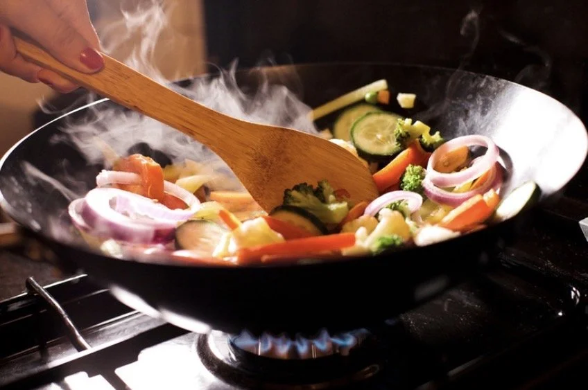 Hand stir-frying colorful vegetables in a wok over a gas flame.