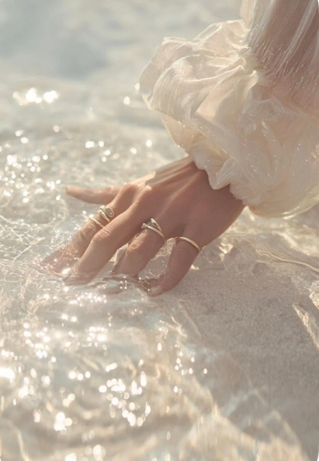Hand mit Ringen im Wasser am Strand, Sonnenlicht, leichter Schatten.
