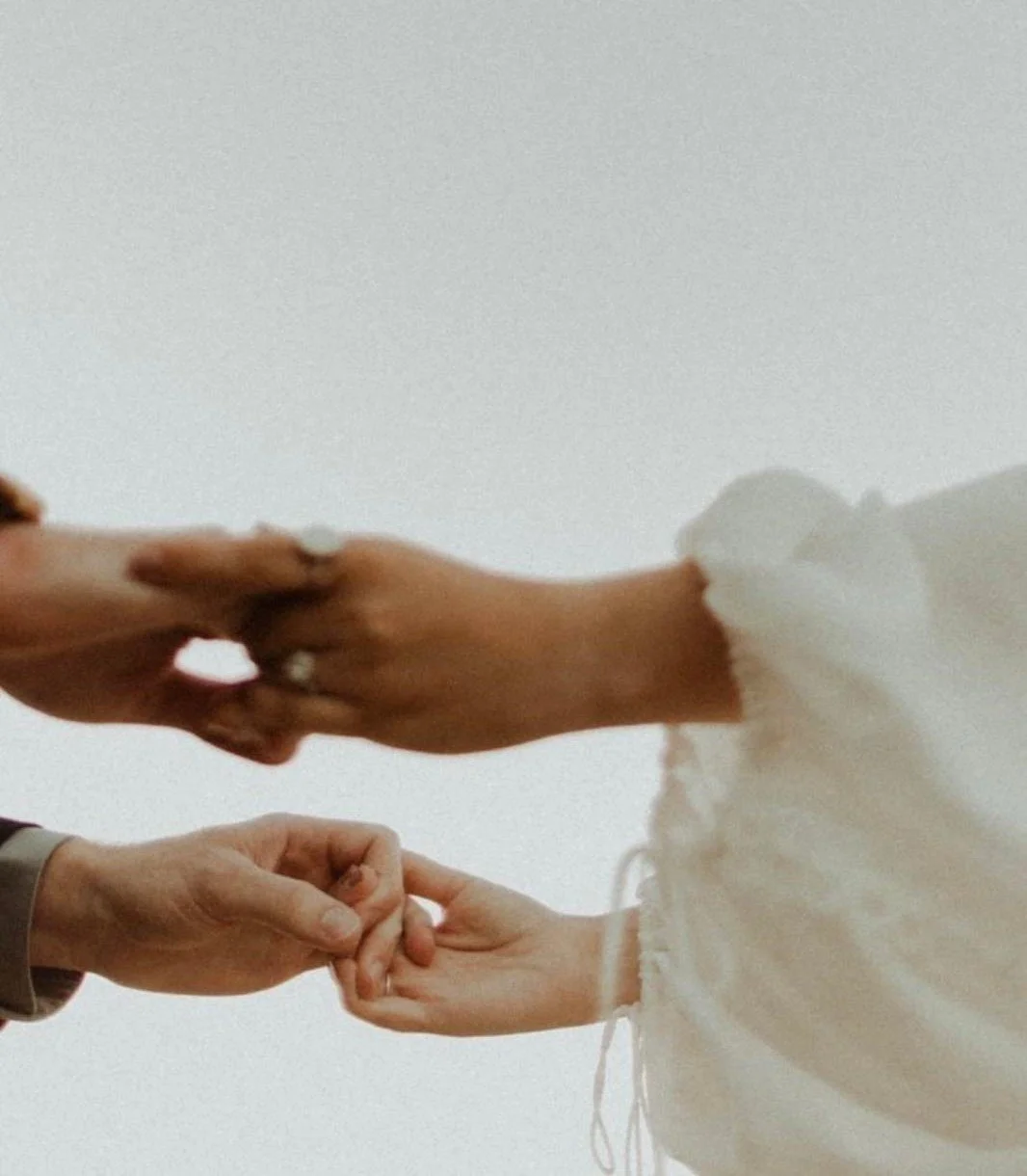 Zwei Personen halten sich an den Händen, eine Person trägt einen weißen, puffigen Ärmel, die andere Person trägt einen grauen Ärmel.