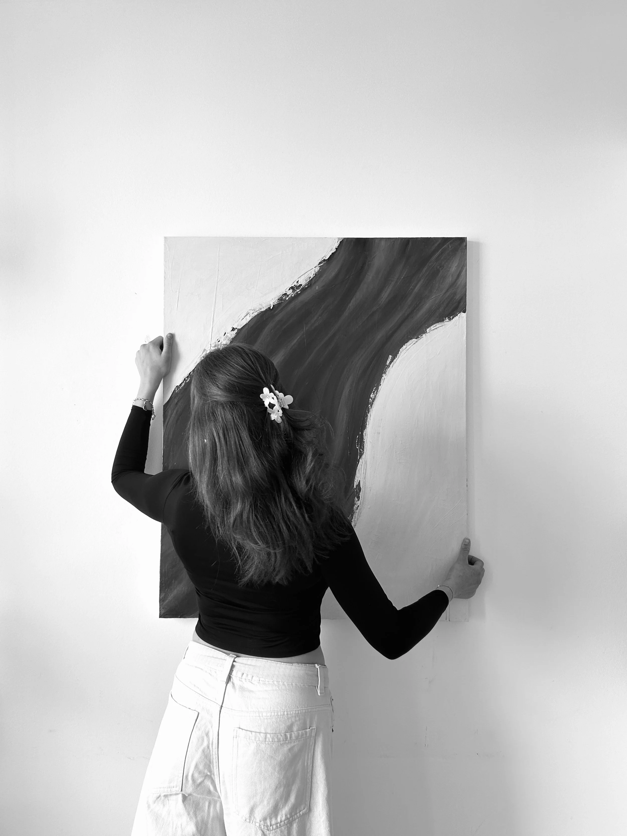 Frau hängt abstraktes schwarzes und weißes Gemälde an eine weiße Wand auf.