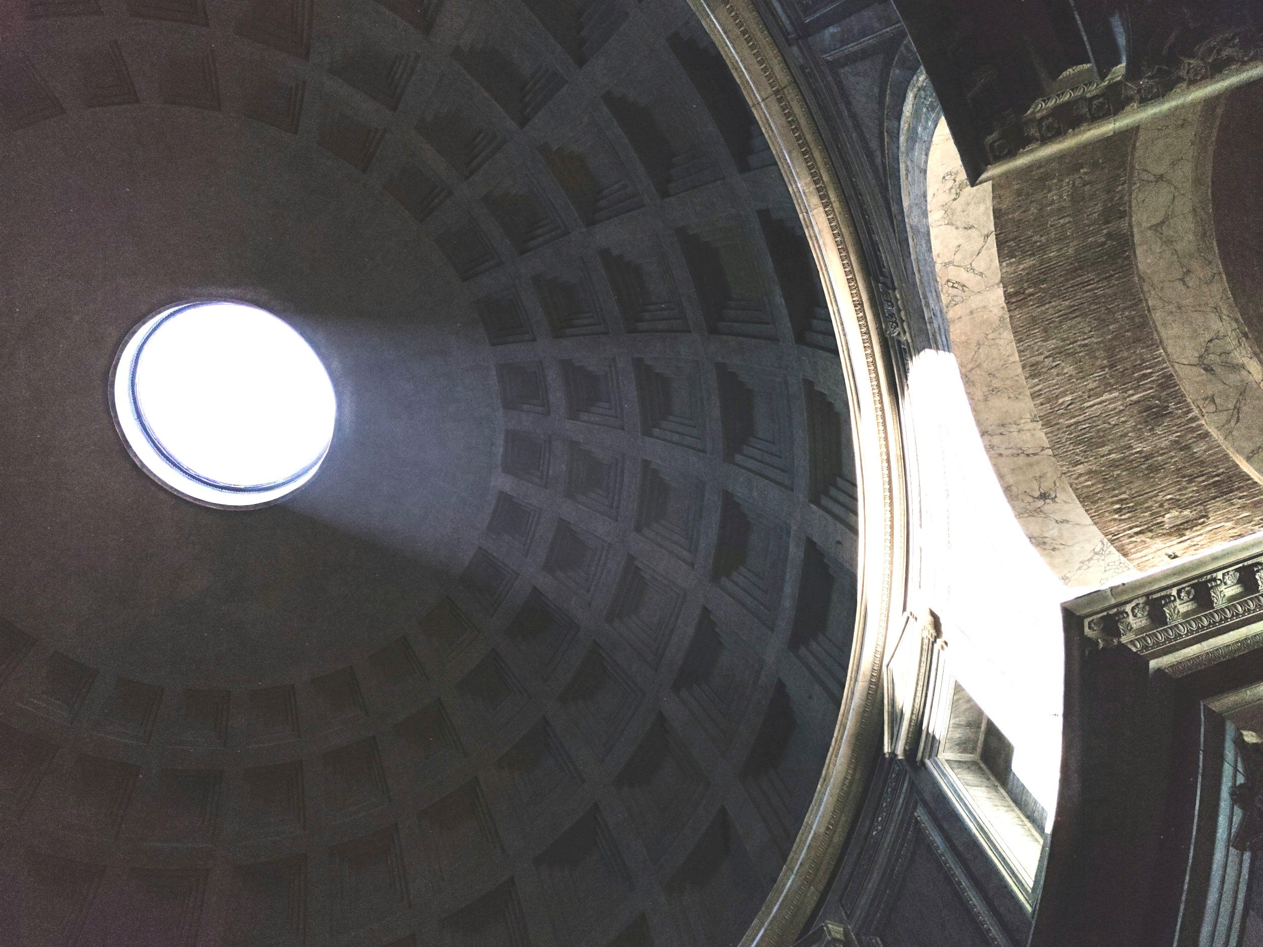 Interior view of the dome of the United States Capitol building with sunlight shining through an oculus at the center, featuring ornate architectural details and marble accents.