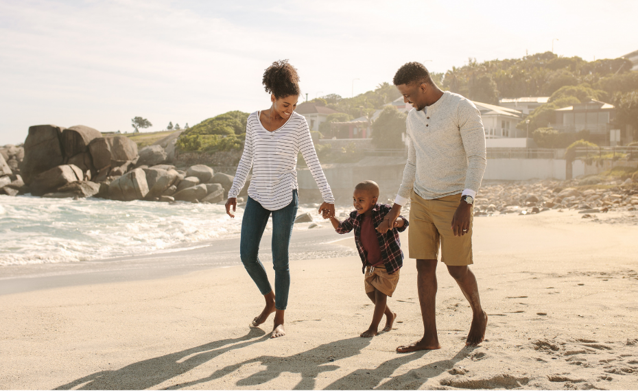 A happy family of three walking hand in hand on the beach, smiling and enjoying the sunny day.