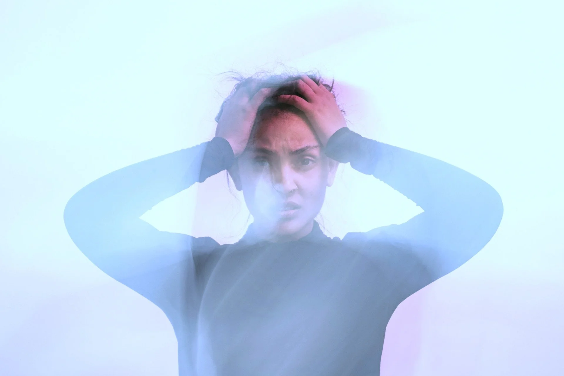 A young woman with hands on her head looking overwhelmed, with a blurred, confused quality to the photo
