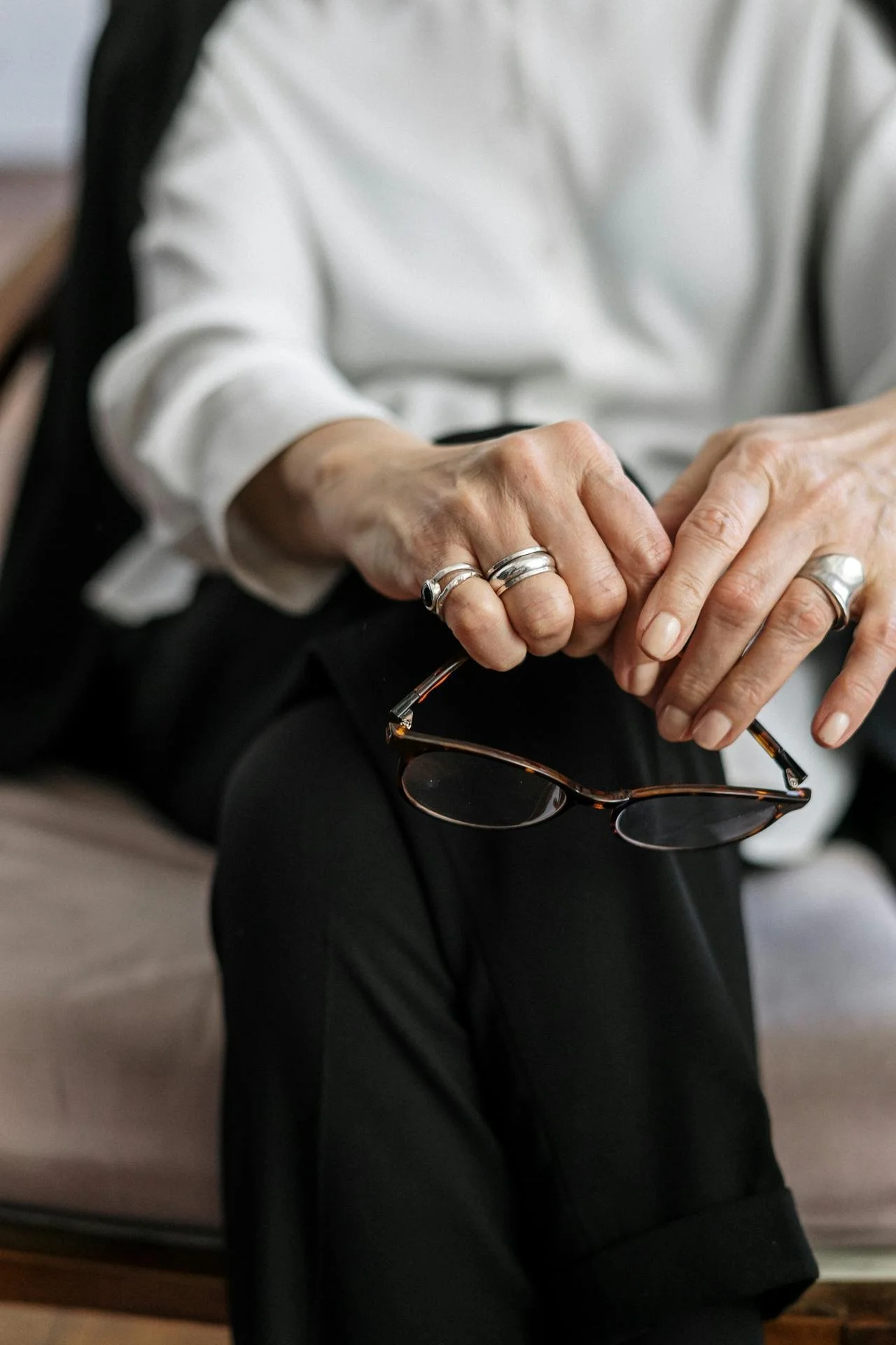 Close of up a woman’s hands resting on crossed legs and holding a pair of glasses