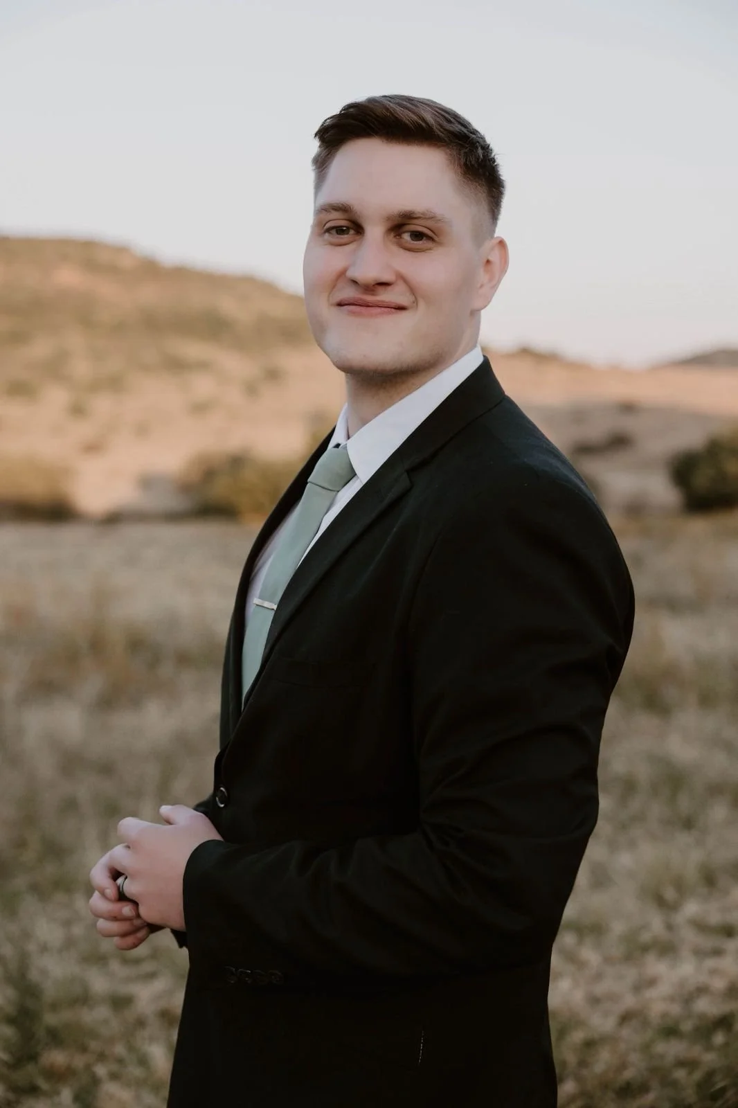 Young man with brown hair and blue eyes smiling, wearing a blue tank top, at the gym.