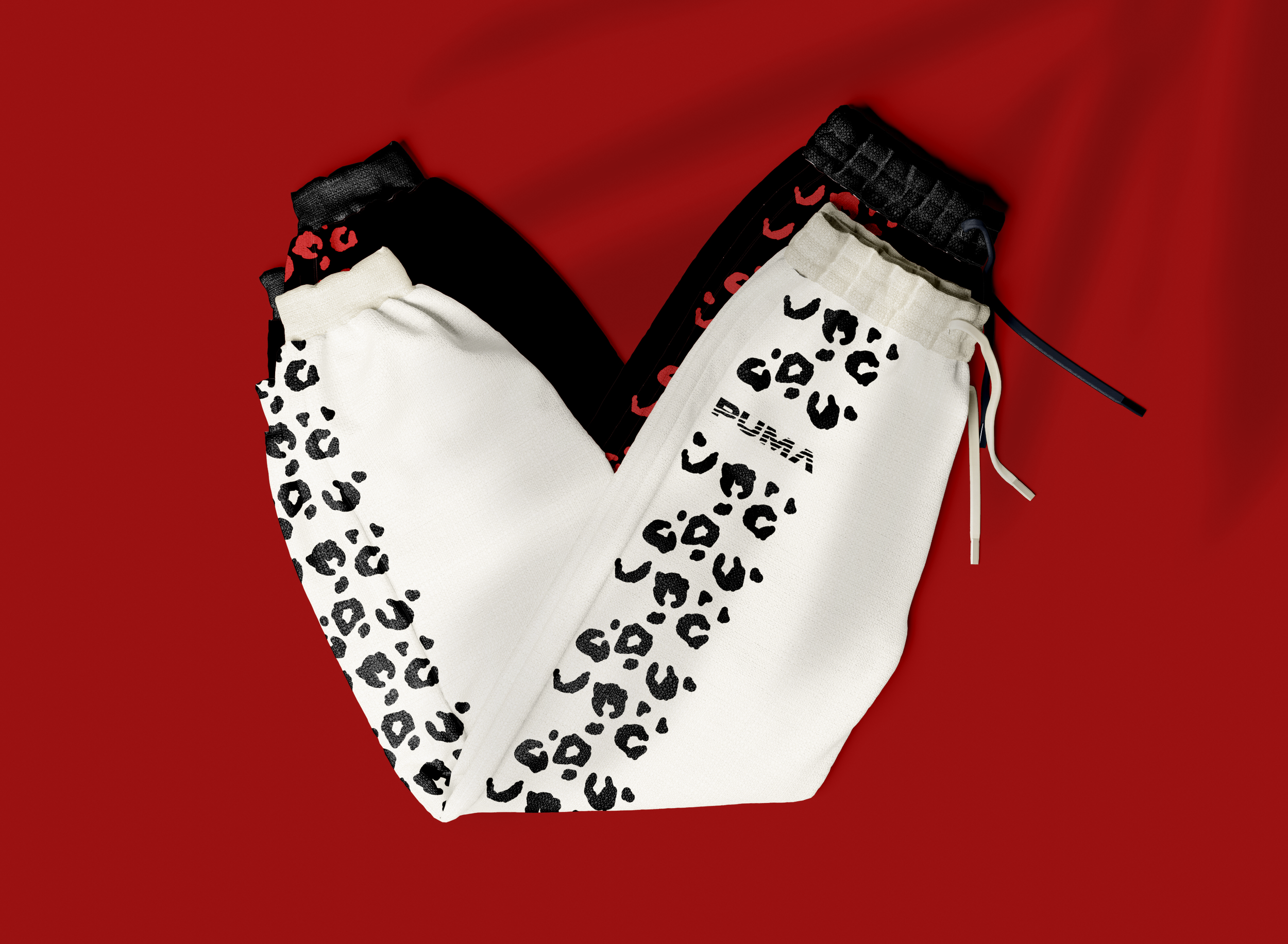 A pair of Puma sweatpants with a black and red leopard print pattern, and a separate white pair with black leopard print and Puma logo, displayed on a red background.