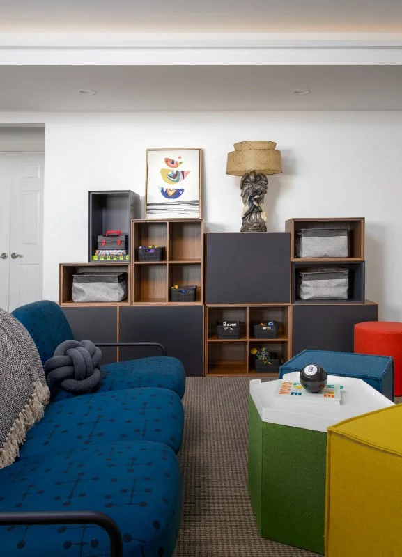 Living room with colorful furniture, modern decor, and storage unit against white wall with artwork and lamp.