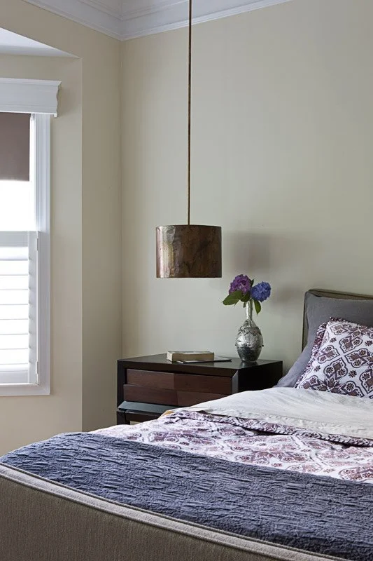 Bedroom with a bed, a nightstand with a flower vase, a book, and a pendant light hanging from the ceiling.