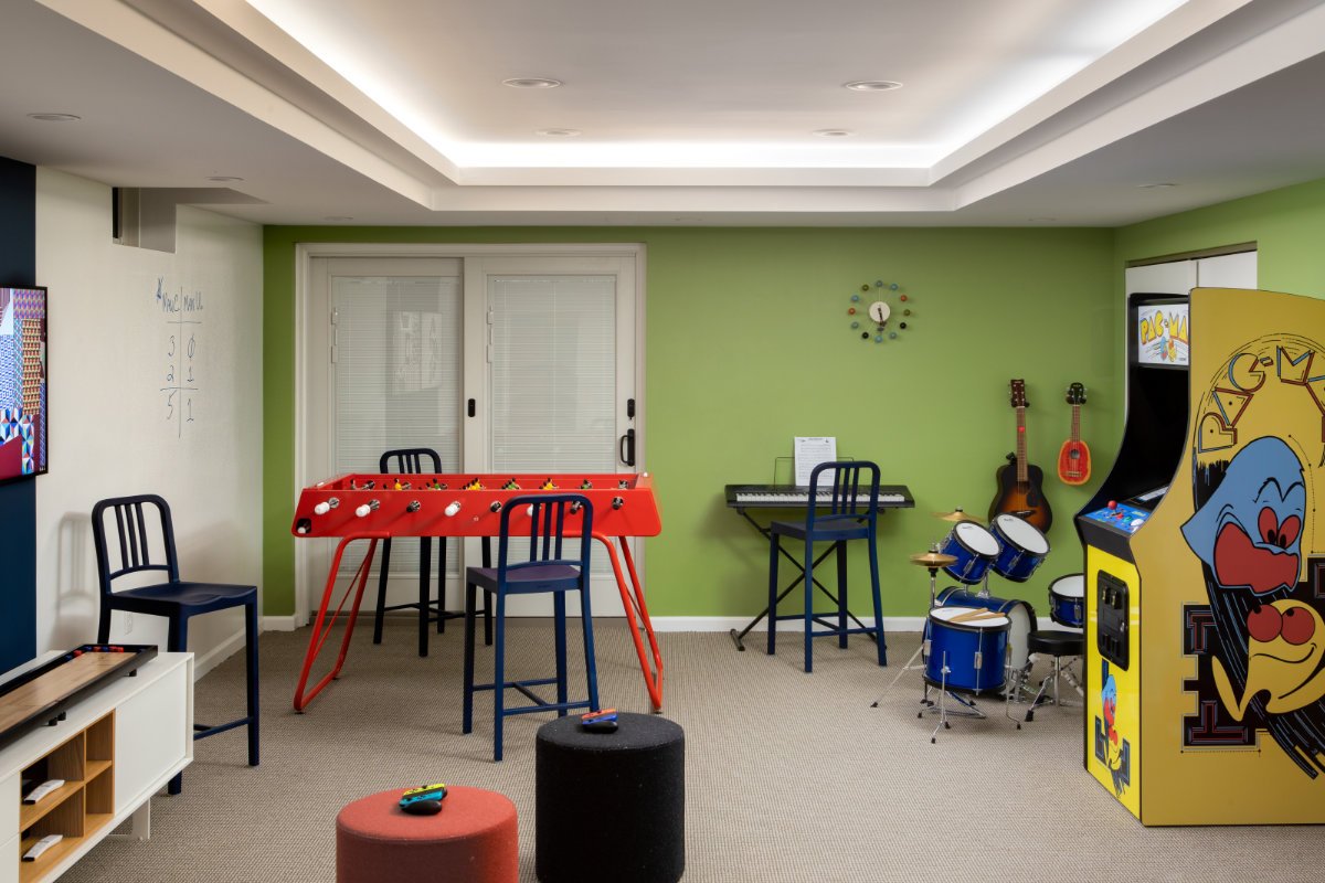 Game room with foosball table, drum set, guitars, arcade game, and kids' furniture.