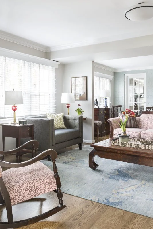 Living room with sofas, armchair, coffee table, end table with lamps, a sideboard, and a rug, with windows and a glass door in the background.