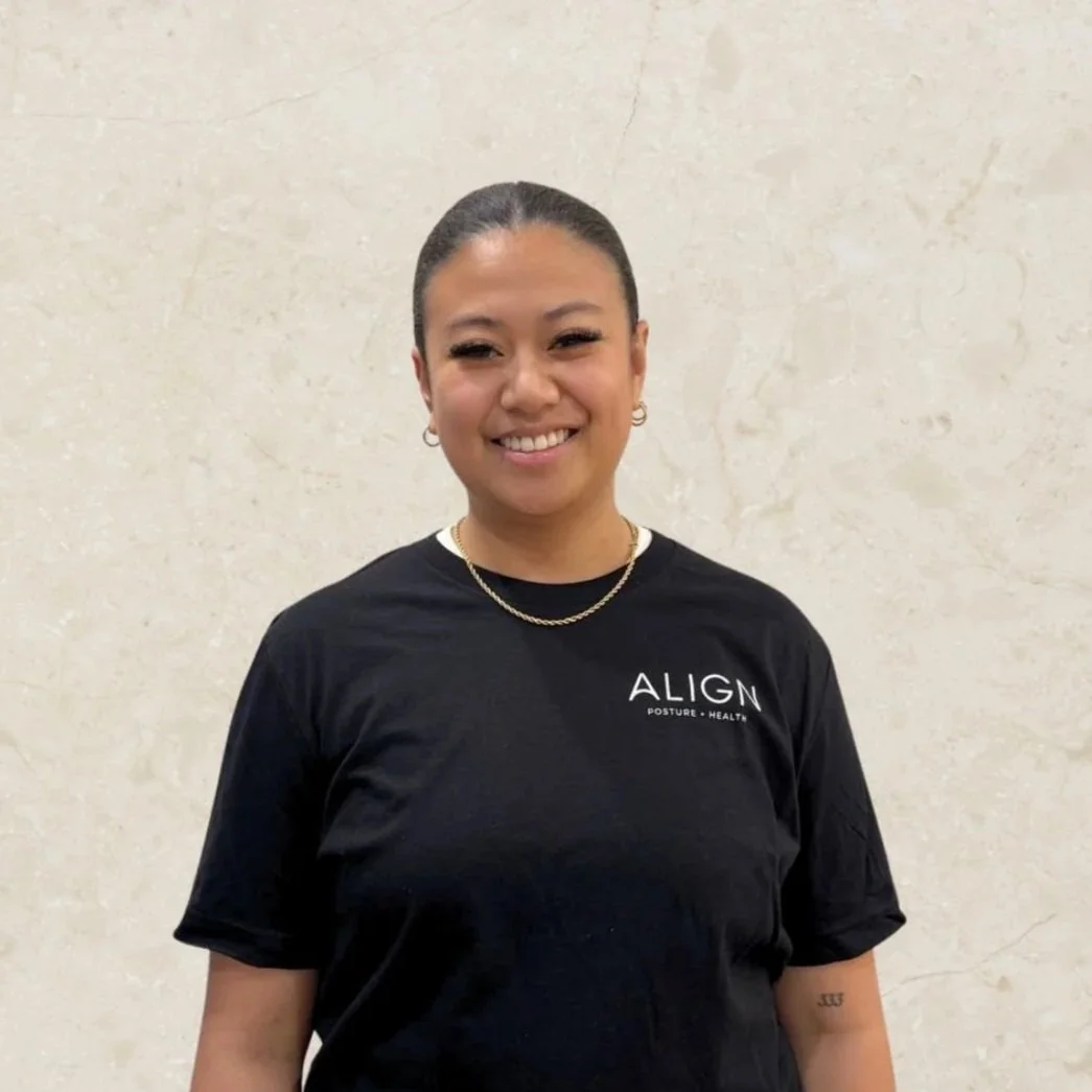 Smiling person wearing a black "Align Posture + Health" t-shirt, against a light-colored wall.