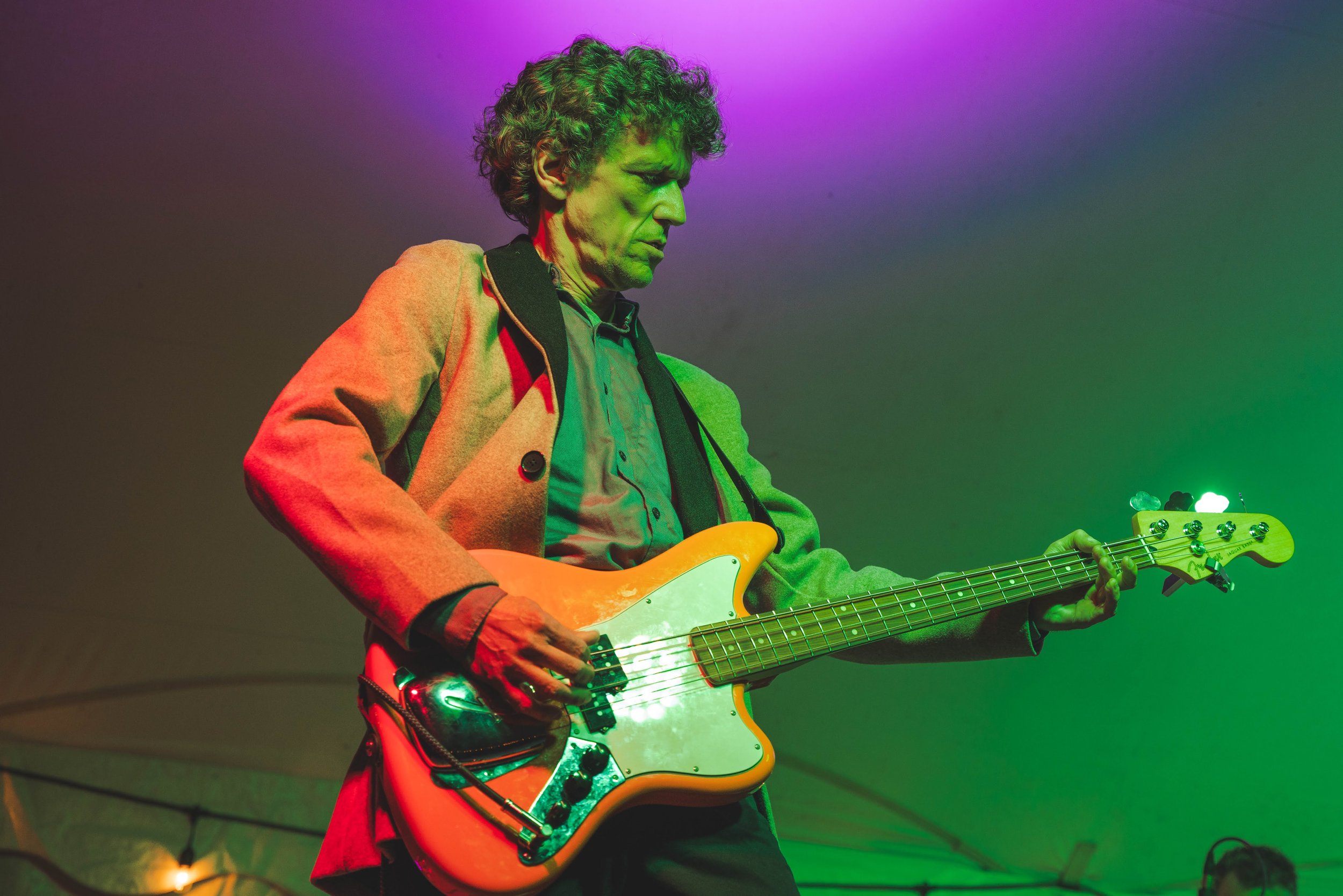 A man playing an electric bass guitar on stage under colorful lighting