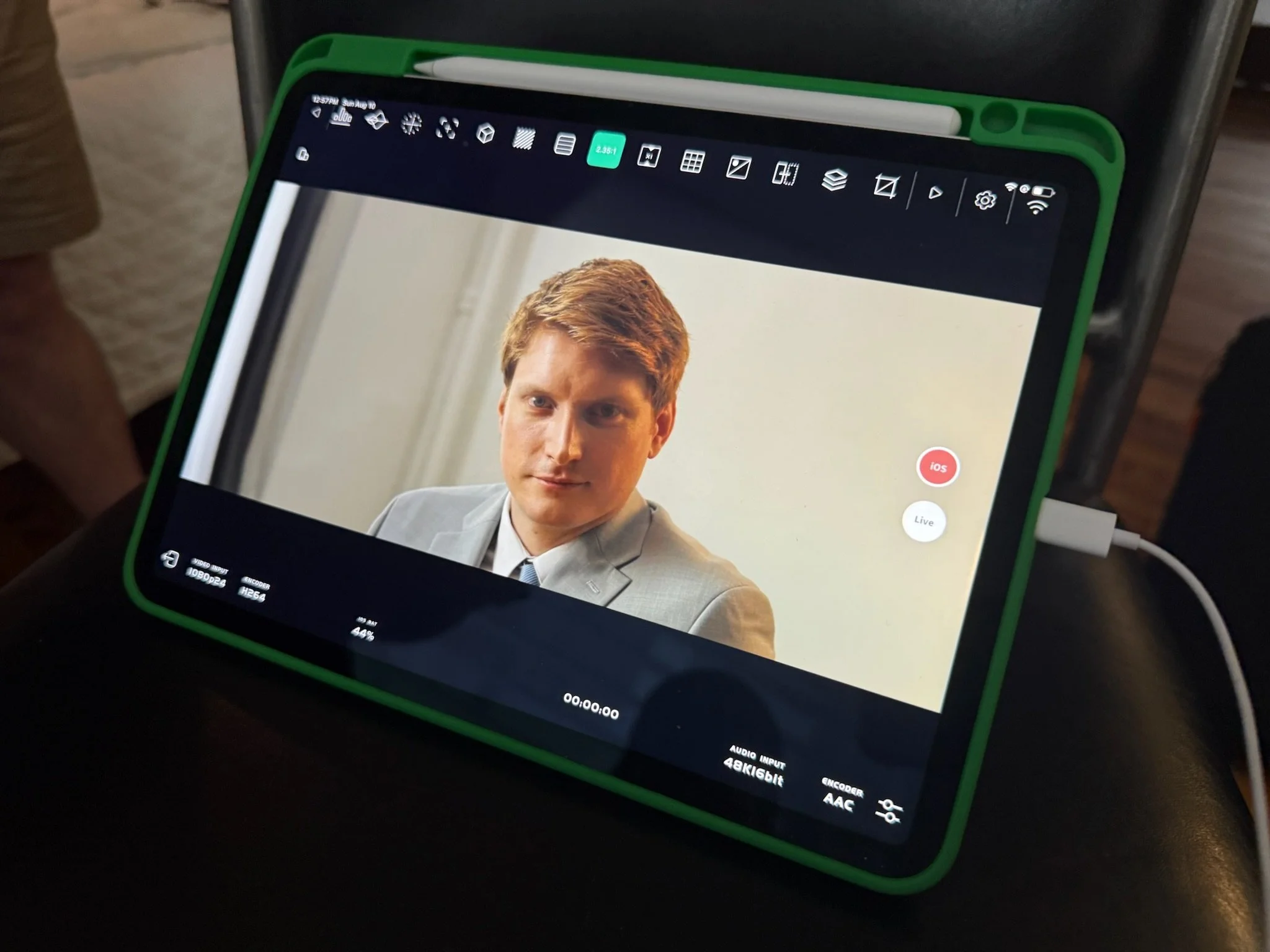 A tablet with a green frame displaying a video recording of a man in a gray suit and white shirt, with editing interface icons visible on the screen.