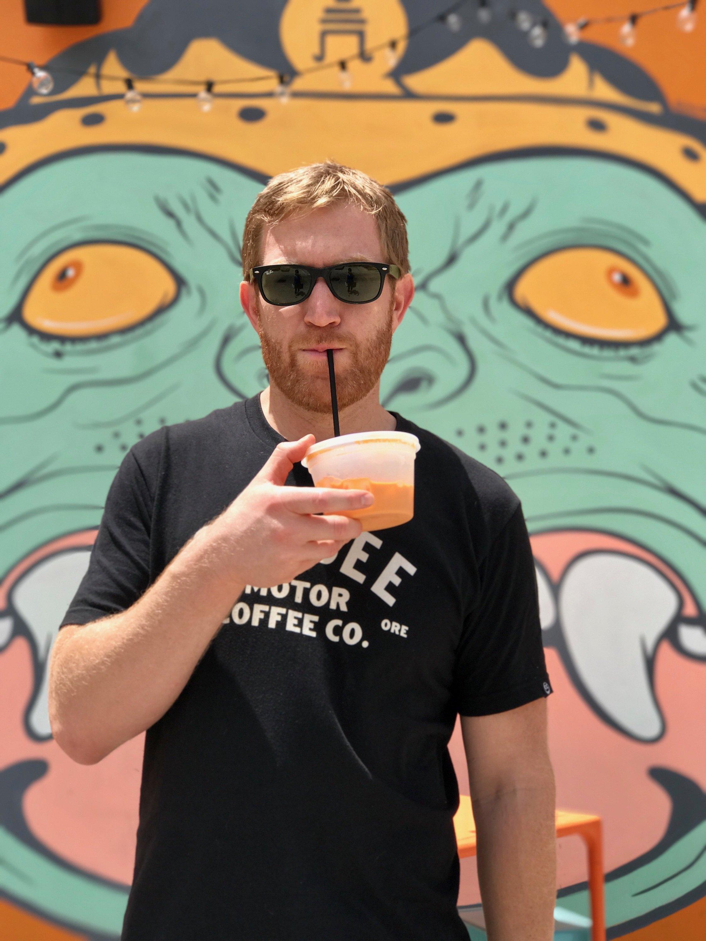 Man in sunglasses drinking from cup in front of colorful mural