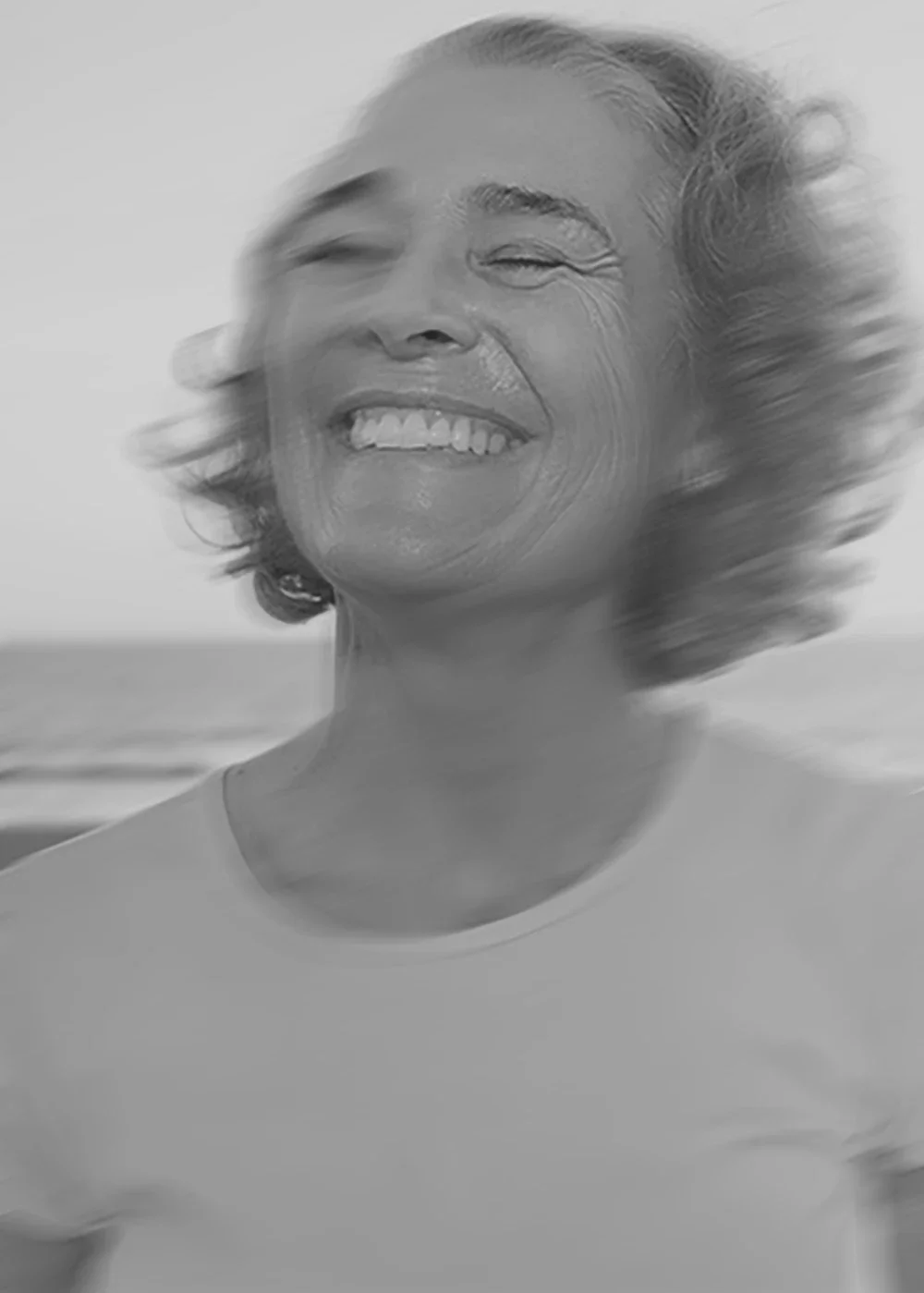 A woman with short, wavy hair smiling and looking slightly to the side, outdoors near the water.