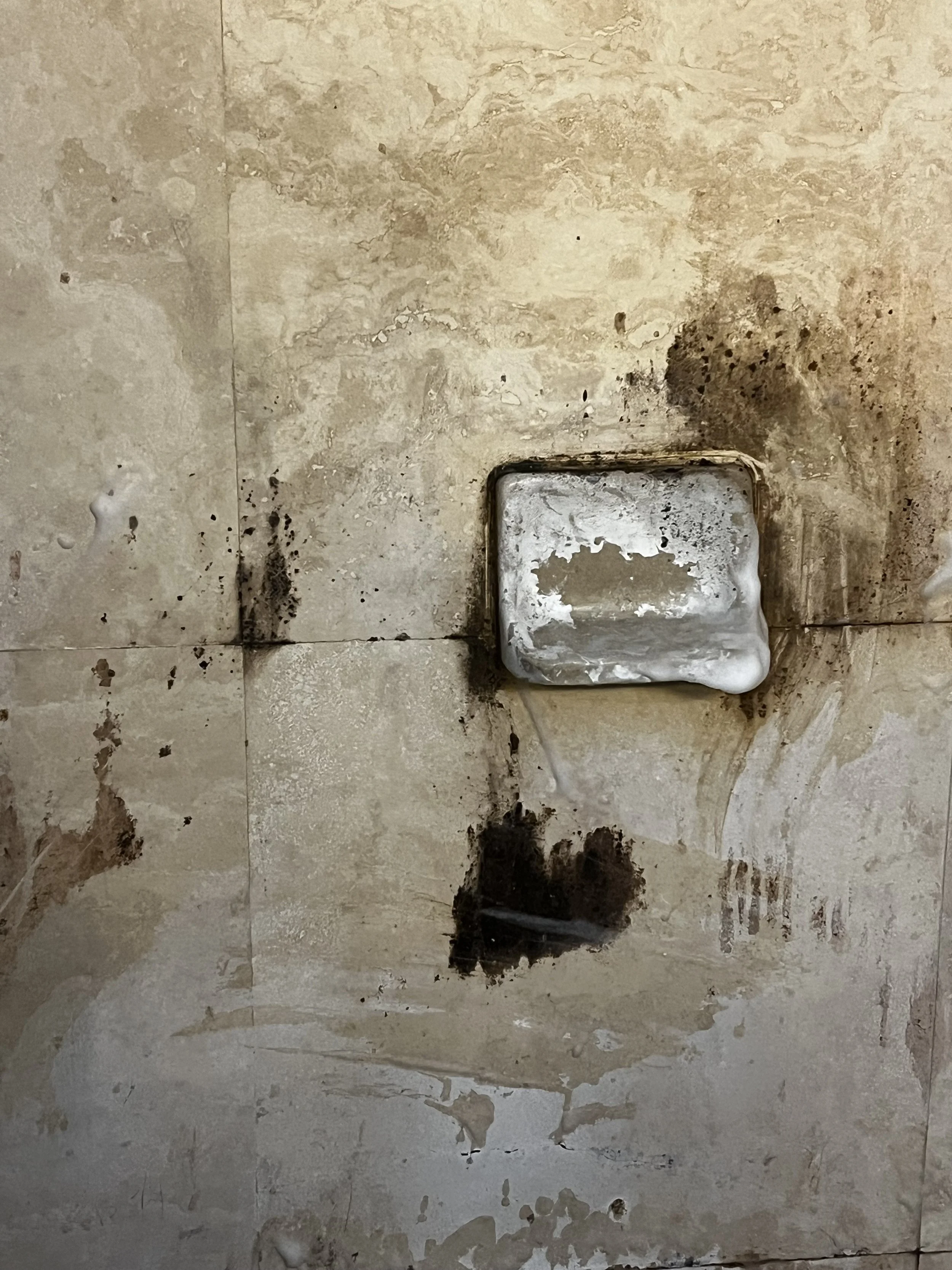 A dirty tiled floor with a metal drain cap, some black grime around it, and soapy residue.