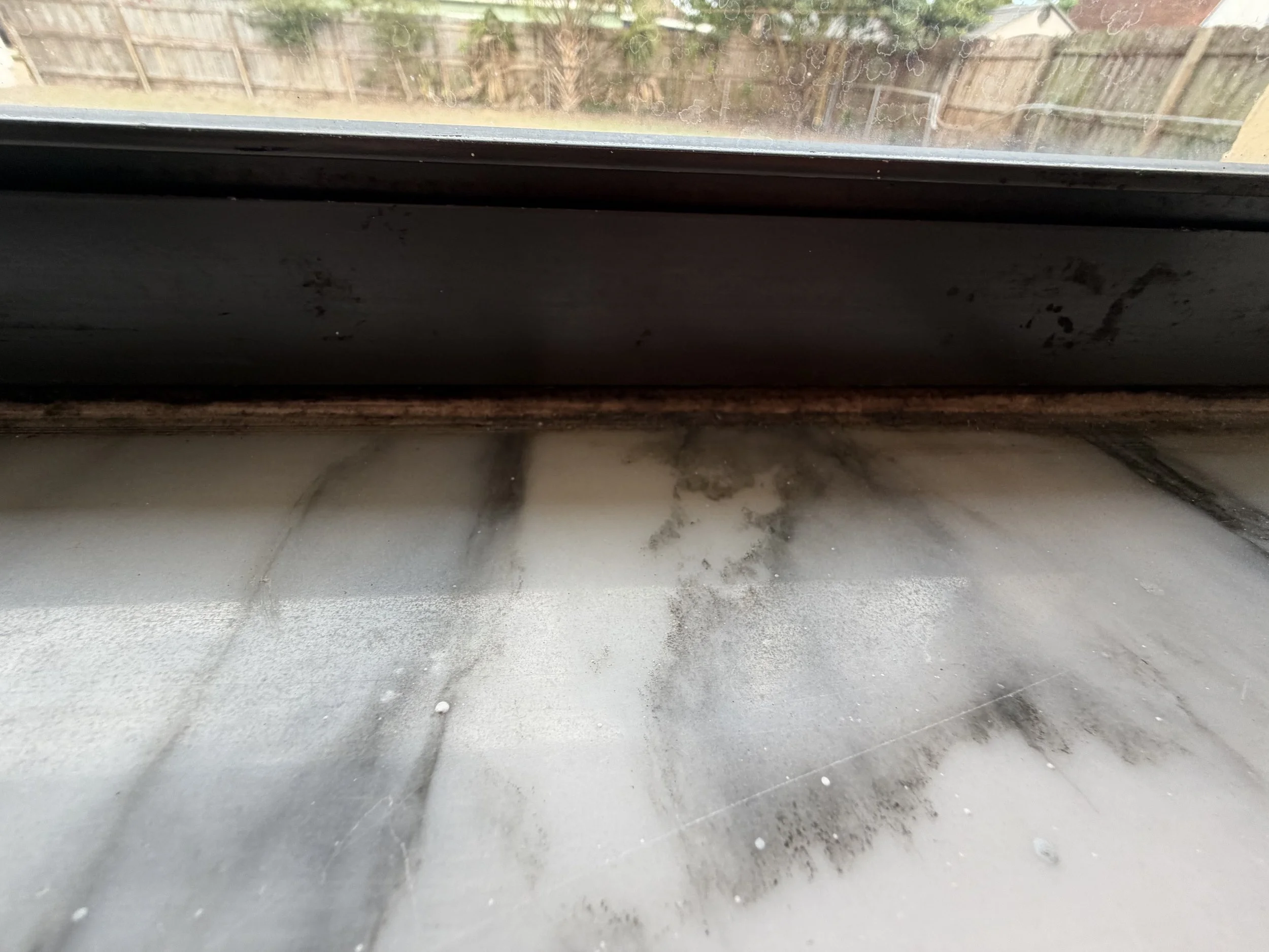 Close-up of a dusty and dirty windowsill with some grime and streaks, the caulk is molded/mildewed to a dark brown color.