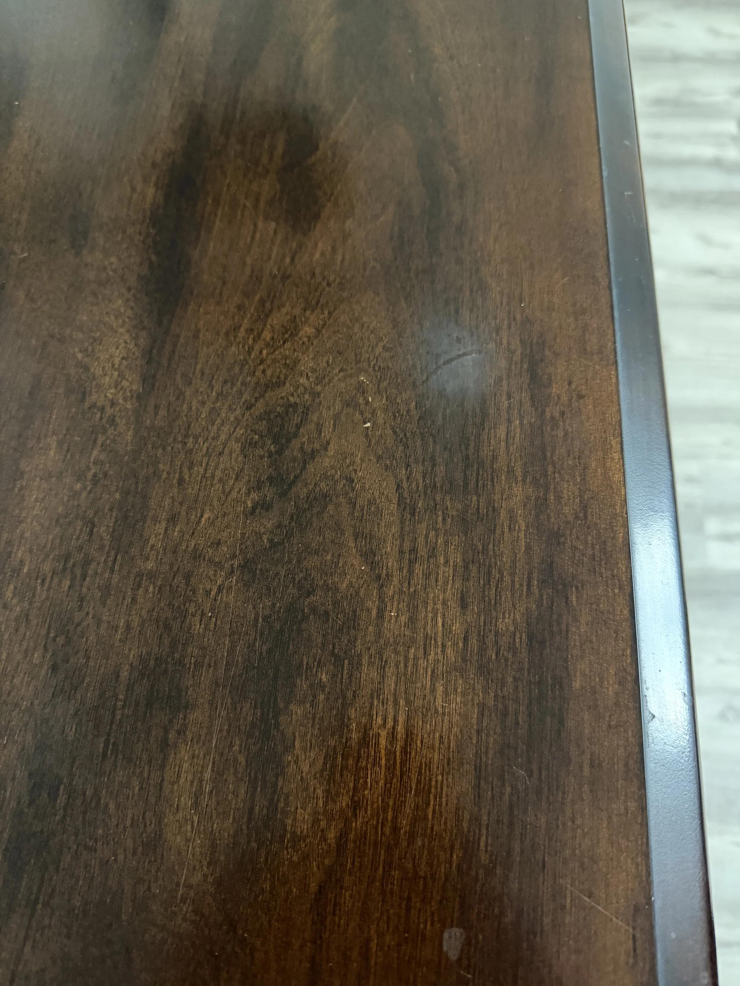 Close-up of a dark brown wooden surface with visible wood grain and a small rectangular scratch near the right edge.