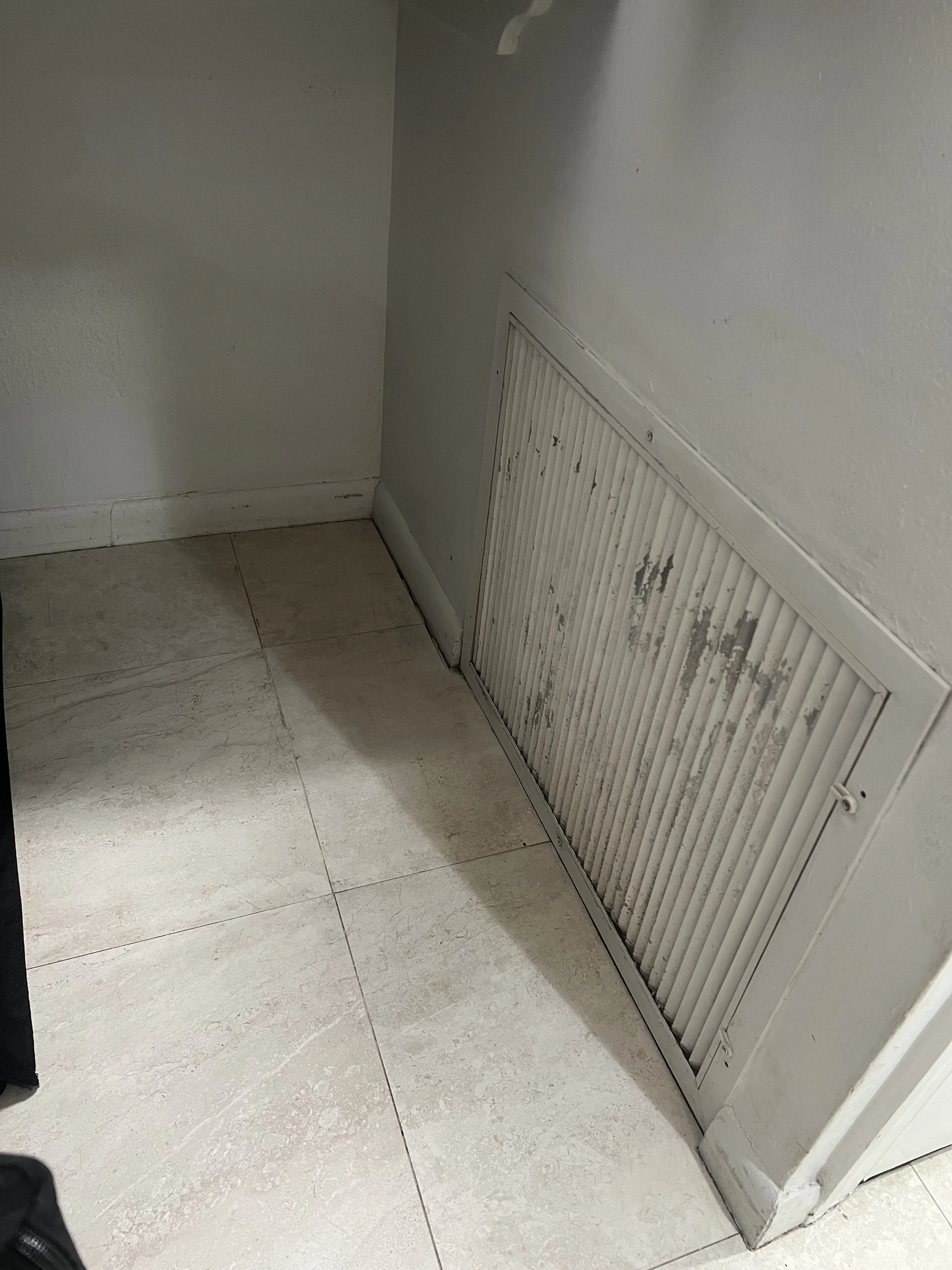 A close-up of a white wall with a metal vent cover near the floor, showing some need for fresh paint but otherwise completely clean of any dust or dirt.