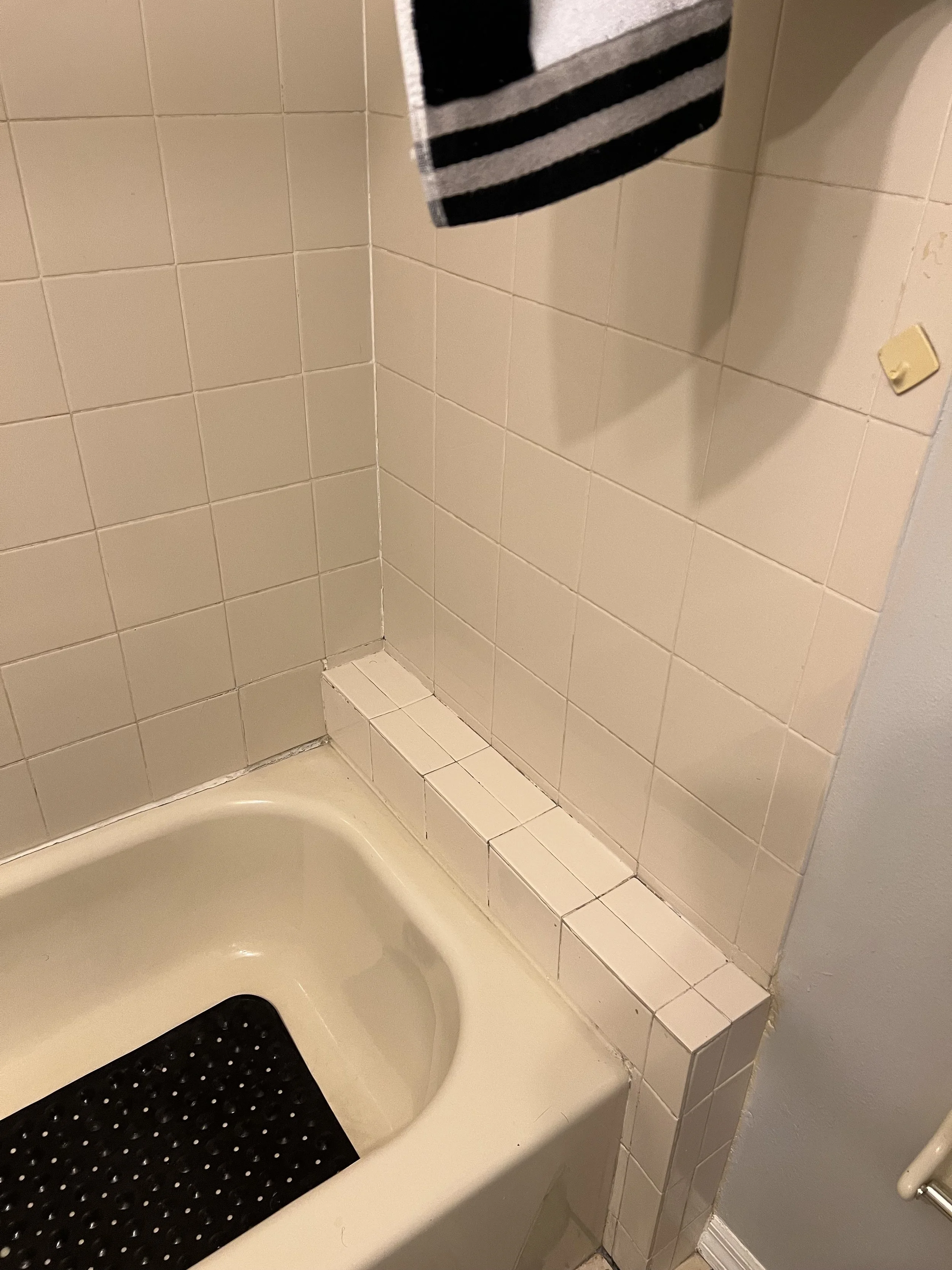 Close-up of a bathroom corner with a bathtub, tiled walls, and a black anti-slip mat in the tub.